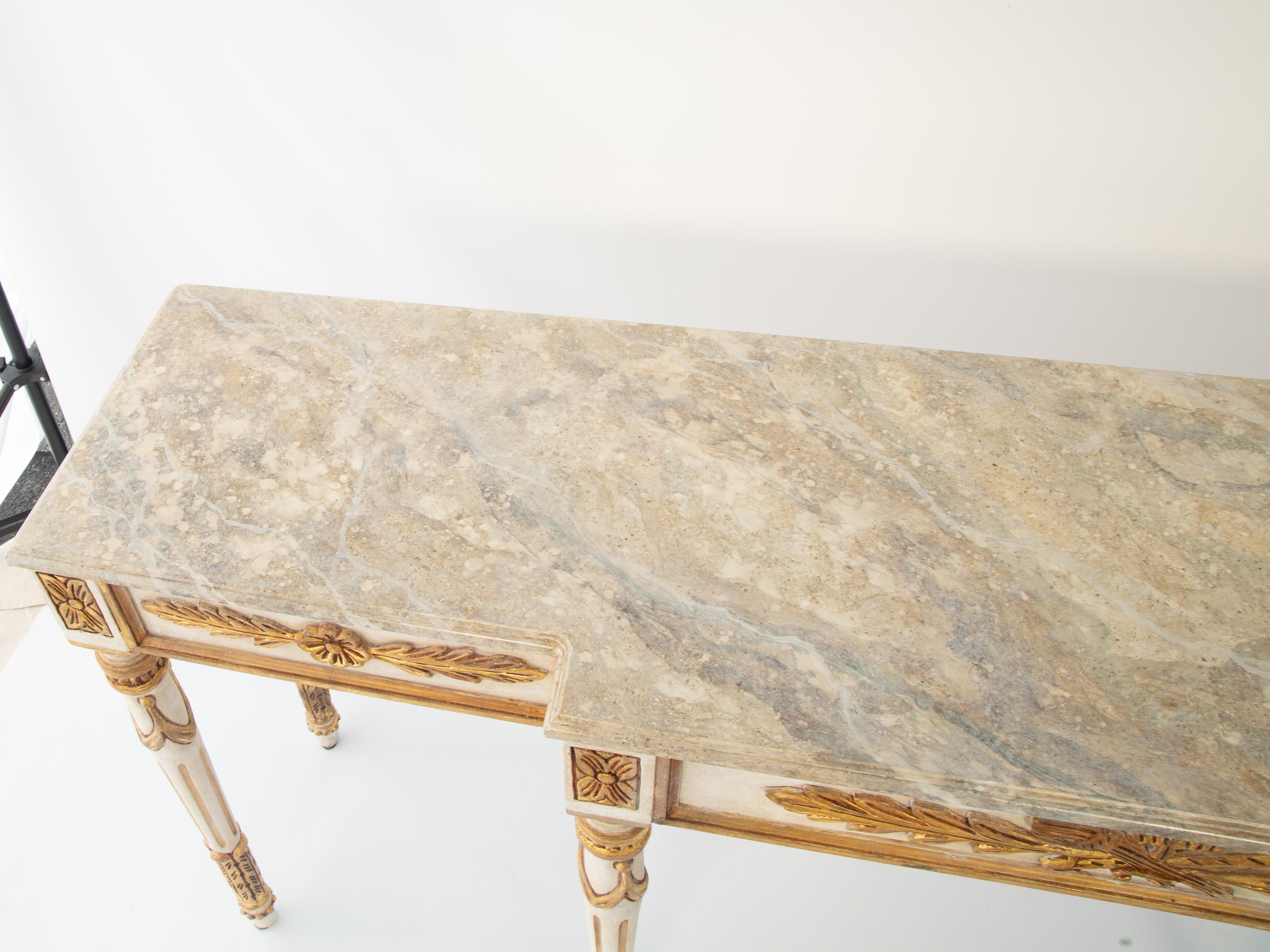 Konsolentisch mit langen und schmalen Proportionen, im Louis XVI-Stil. Der Tisch mit cremefarbener und paketvergoldeter Oberfläche weist natürliche Abnutzungserscheinungen auf. Die feldförmige Schürze ist mit Rosetten, Akanthus und klassischen