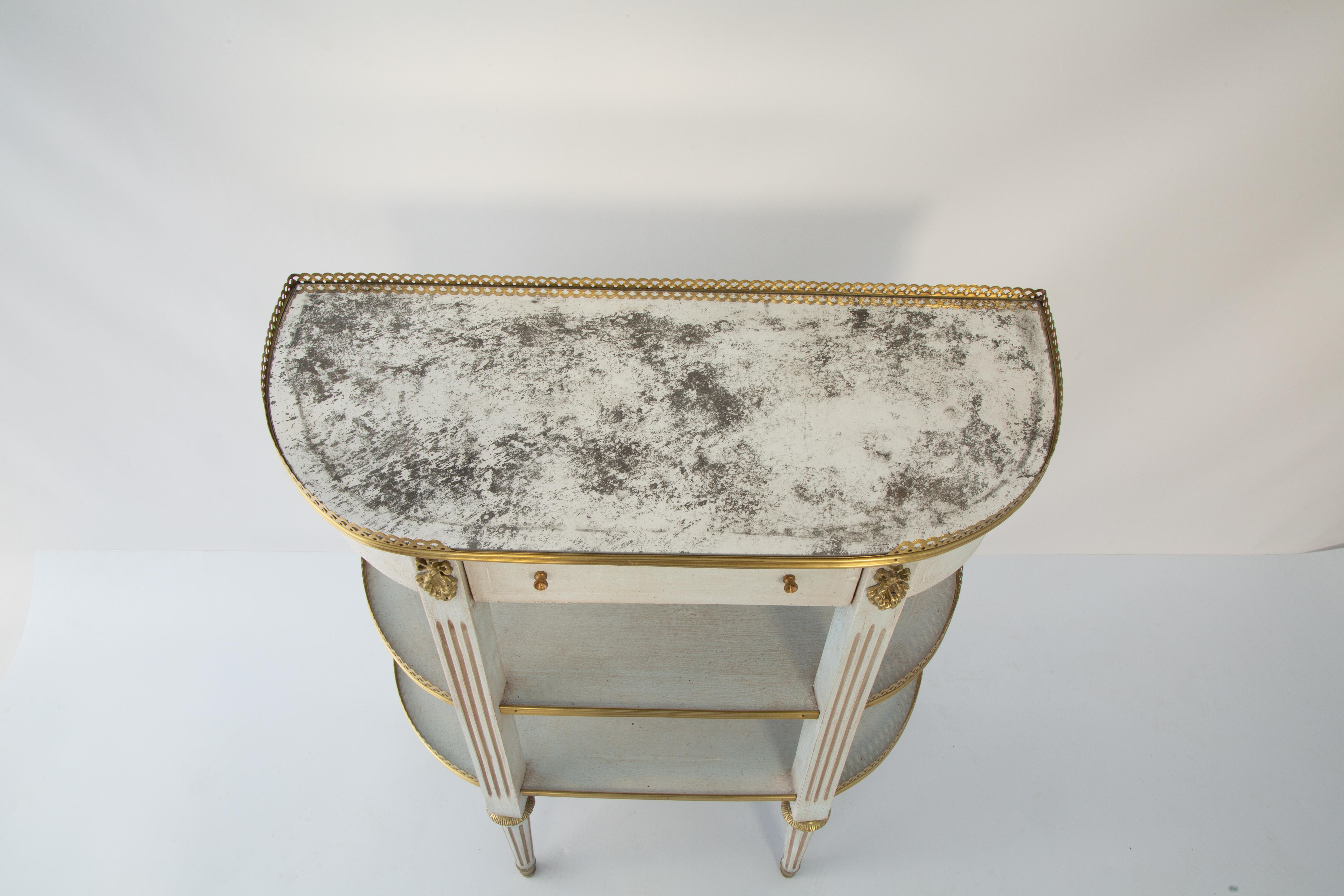 Dreistöckiger Konsolentisch im Louis XVI-Stil mit einer D-förmigen, antik verspiegelten Platte, die von einer zu 3/4 durchbrochenen Galerie eingefasst ist. Das entsprechende Gehäuse mit lackierter Oberfläche und vergoldeten Akzenten. Die Schublade