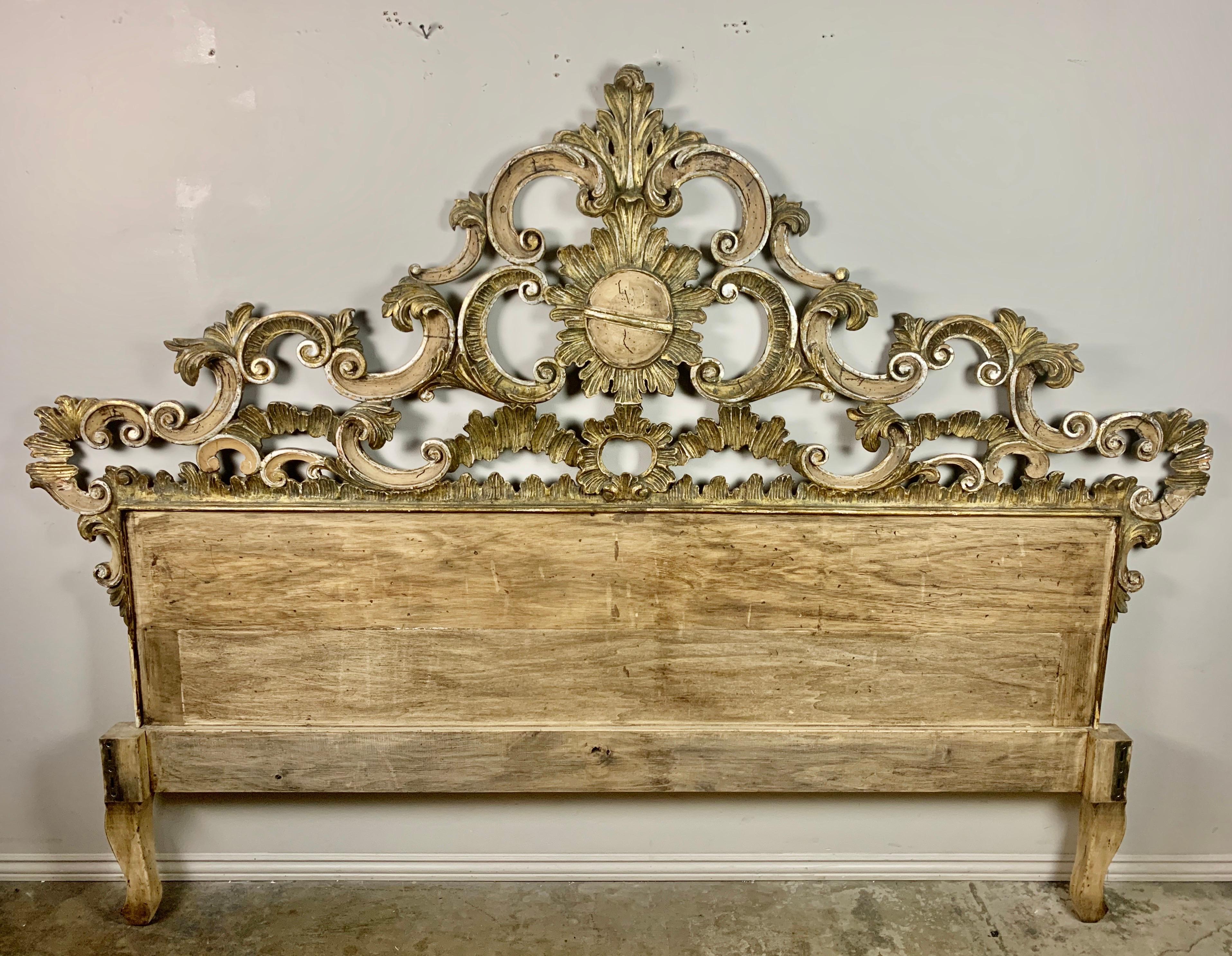 Carved wood Rococo style headboard with a center cartouche surrounded by swirling scrolls and acanthus leaves throughout. The painted and parcel gilt finish on this headboard is beautiful in every way. It is mainly natural bleached wood with