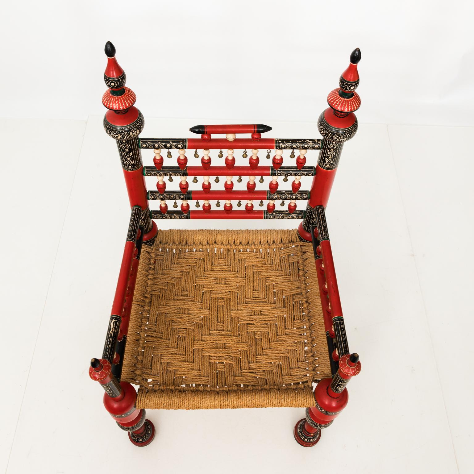 Circa mid-20th century pair of red painted Anglo-Indian style chairs with woven seats and brass bells. Turned spindles are also featured throughout.
 