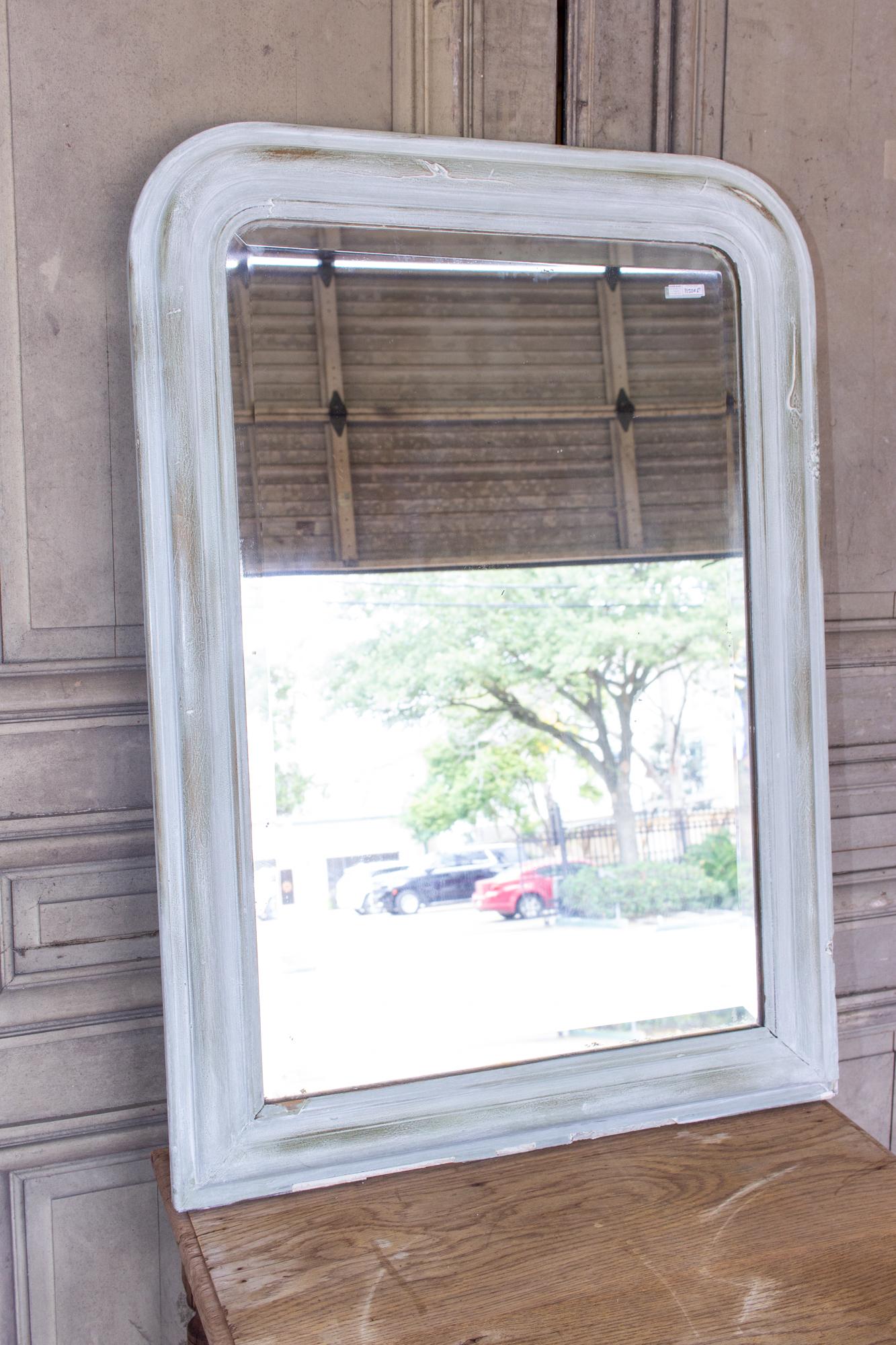 This antique French Louis Philippe mirror has been painted in a light gray color with green and gold accents. The frame is fairly simple, with the Classic lines of a Louis Philippe. The glass is beveled and in good condition, although there is some