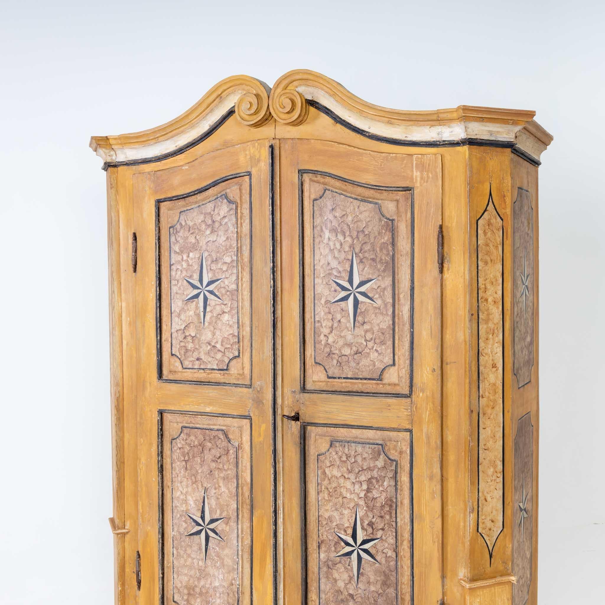 Beveled softwood cabinet with curved gable, beveled corners and two doors. The front and sides are painted in the shape of fillings and decorated with folding stars.