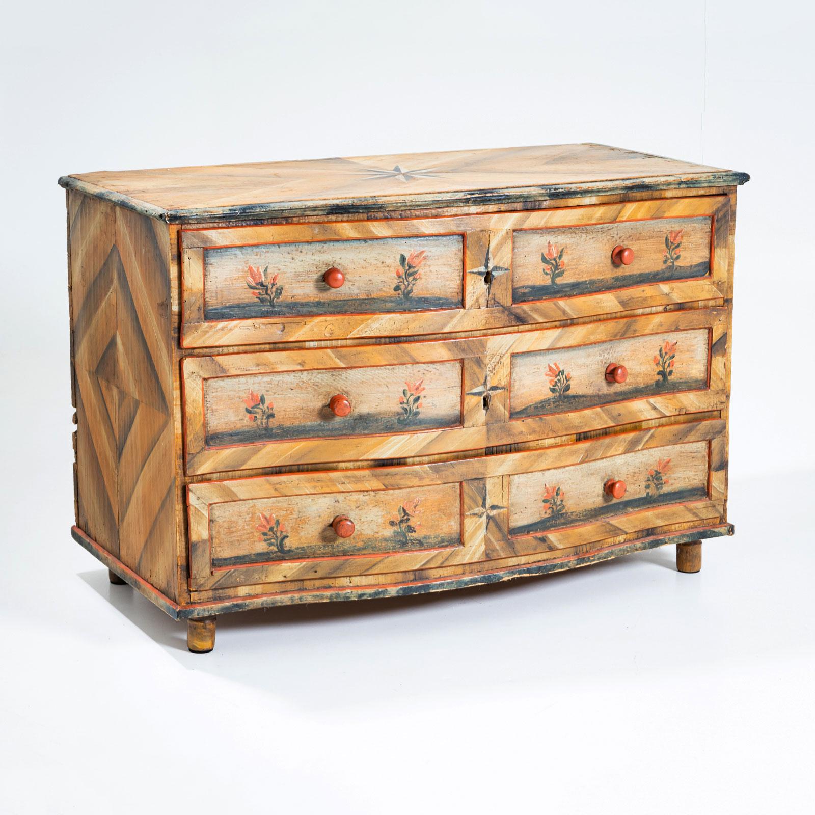 Commodo barocco a tre cassetti con un frontale dolcemente curvo, ornato da stelle pieghevoli intricate e decorazioni floreali dipinte a mano sulle facce dei cassetti. Questi dettagli artistici conferiscono al mobile una presenza affascinante e