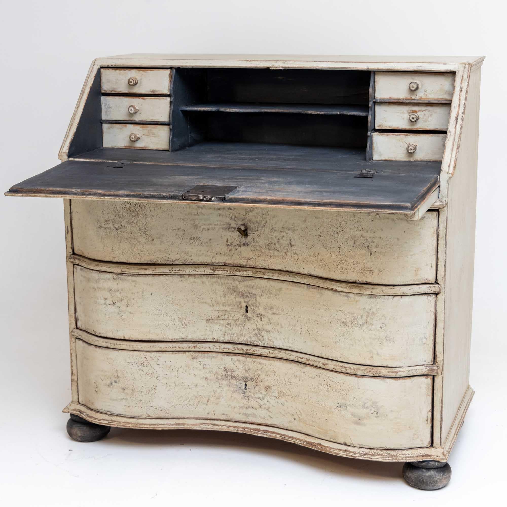 Baroque slanted-flap bureau with curved front and three drawers. The bureau rests on pressed ball feet. The compartments inside consist of six drawers and a shelf. The white painting with dark gray accents is new and has an antique patina.