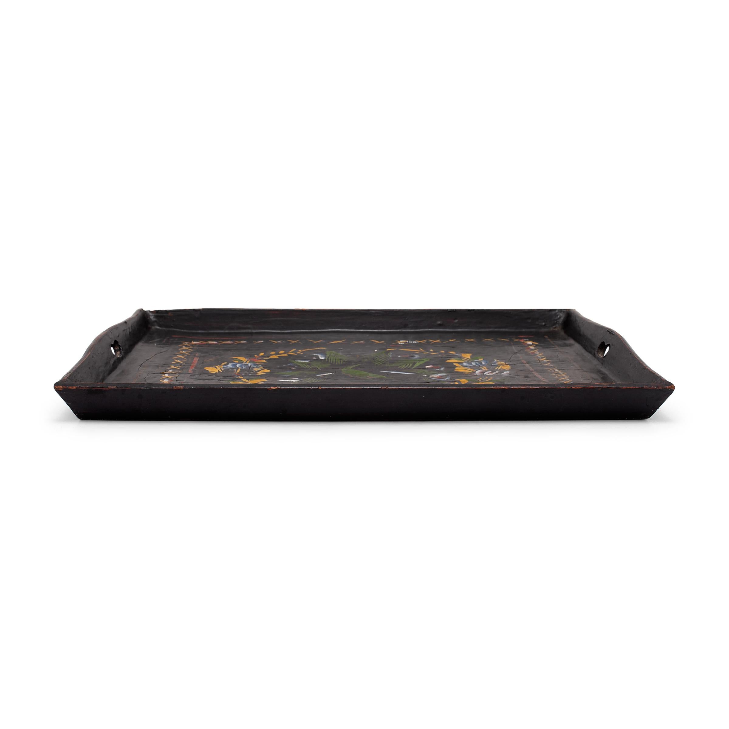 This rectangular wooden tray is finished with black lacquer and decorated with a hand-painted design of flower blossoms and peacock feathers. Painted in a palette of yellow, red, green and blue, the loosely brushed decoration adds bright color and