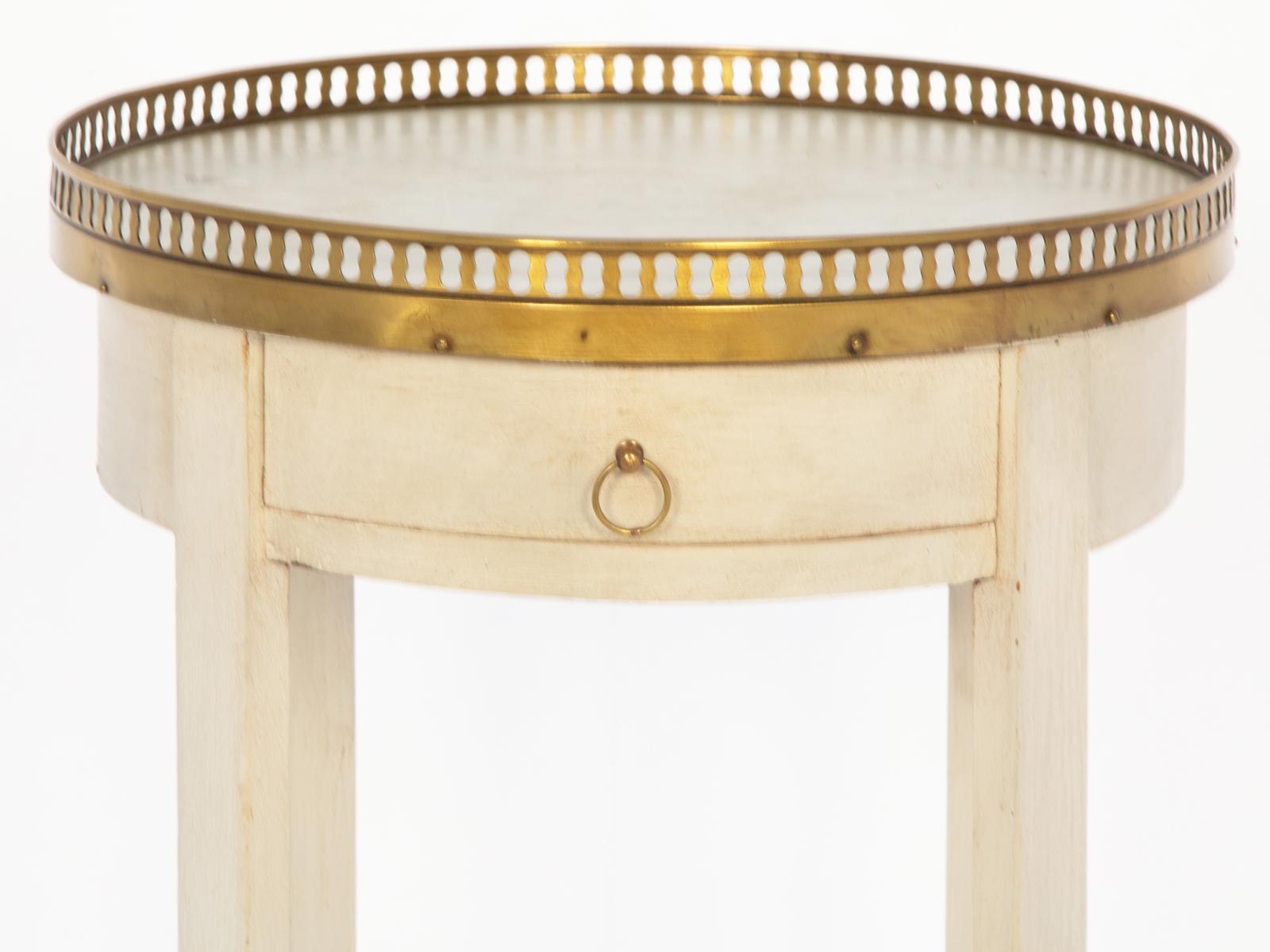 Directoire style candlestand bouiotte table having a round top of marble with pierced brass border, on ivory-painted base, its apron holding a single frieze drawer with ring pull, raised on square-section legs joined by shelf stretcher, ending in