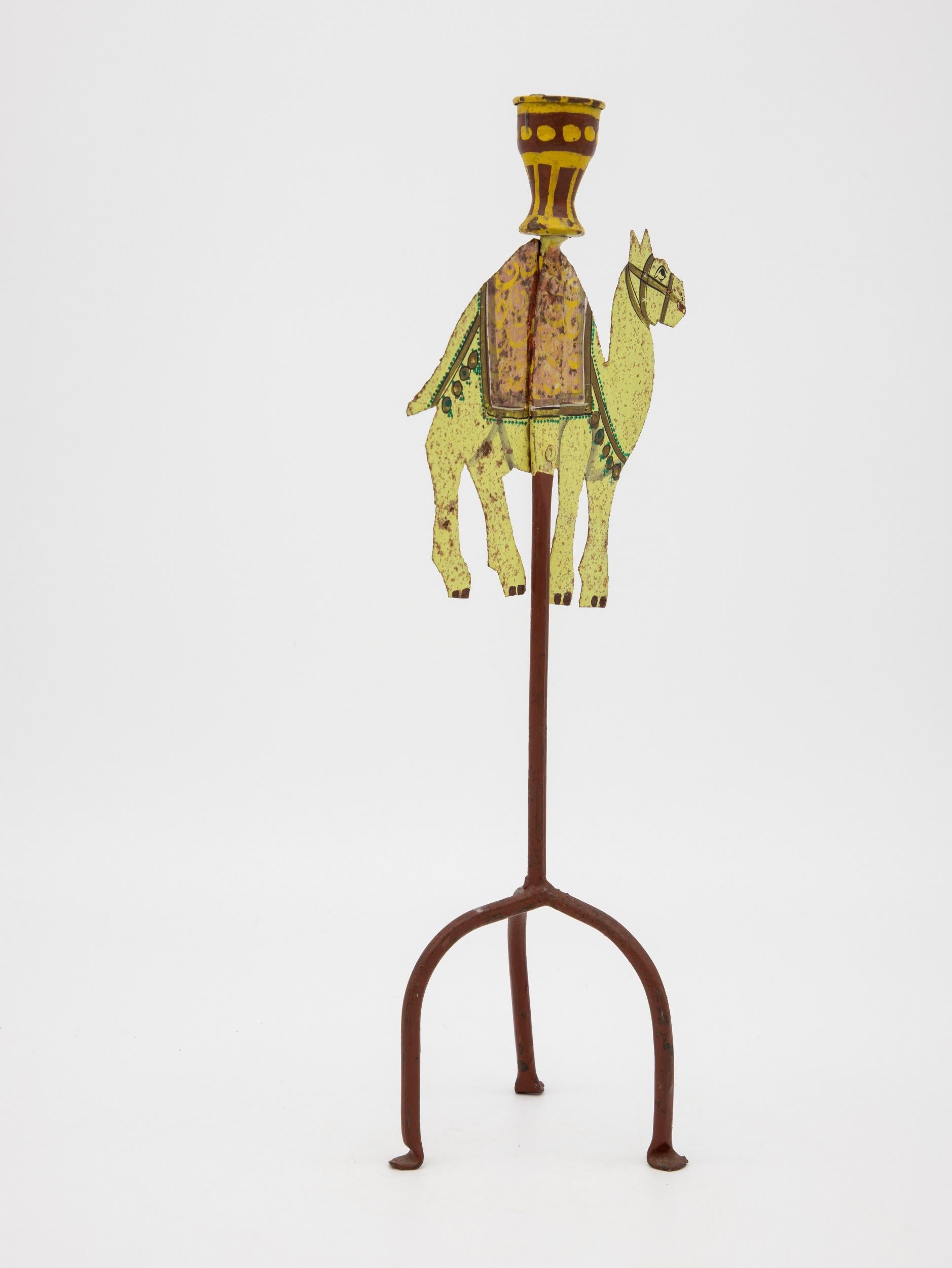 A single metal painted candlestick ca. 1910 in the shape of a camel. This camel is painted in brilliant yellow, red, orange, and green featuring a decorative saddle and bridle. Painted on both sides. Three legs with flat feet.