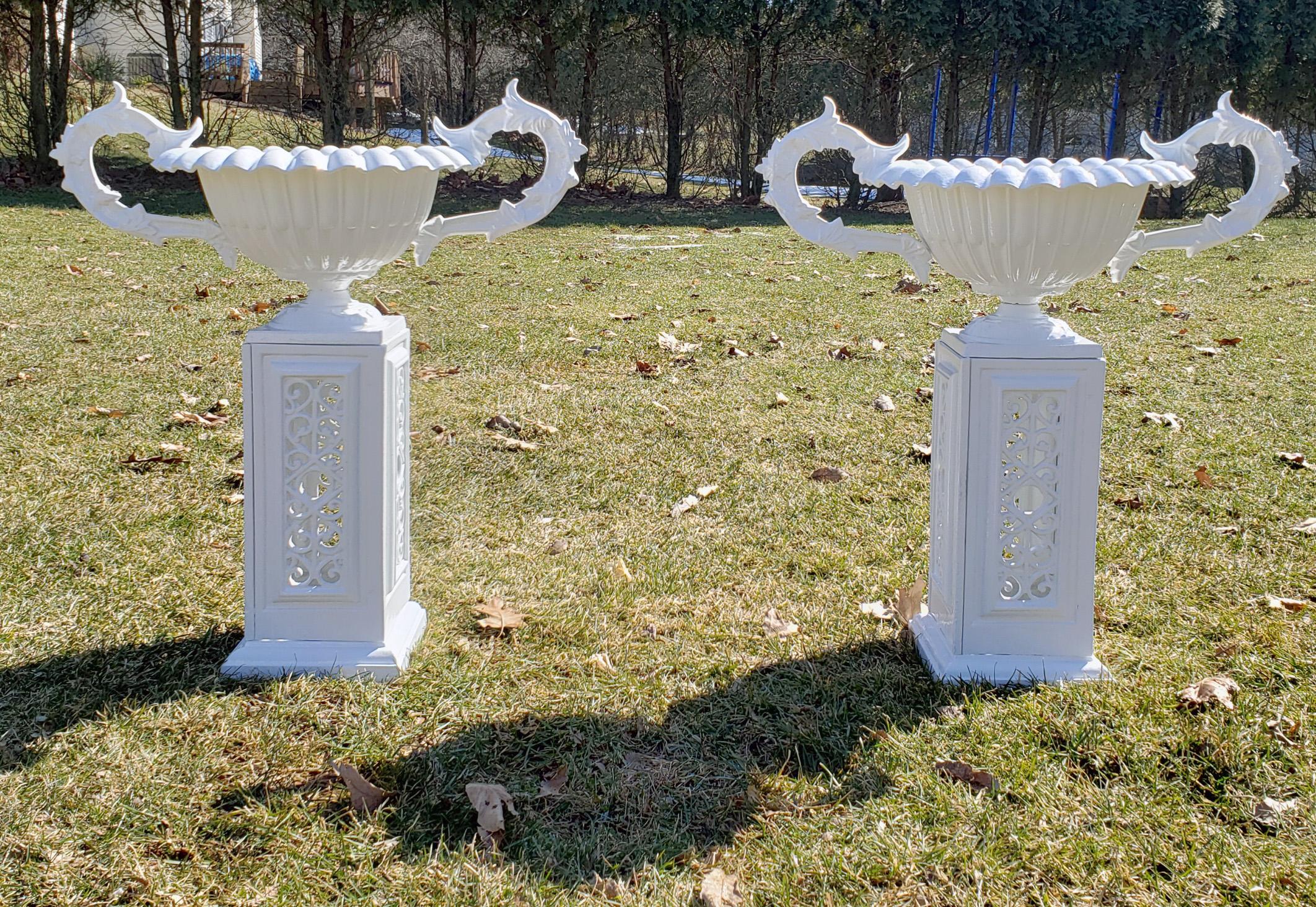 Painted cast iron garden urns and pedestal bases,
American,
mid-20th century.

A pair of white painted cast iron metal urns on square pedestals with the original period finish and oxidized patina. 

The cast iron jardinieres, so-called 'Vase