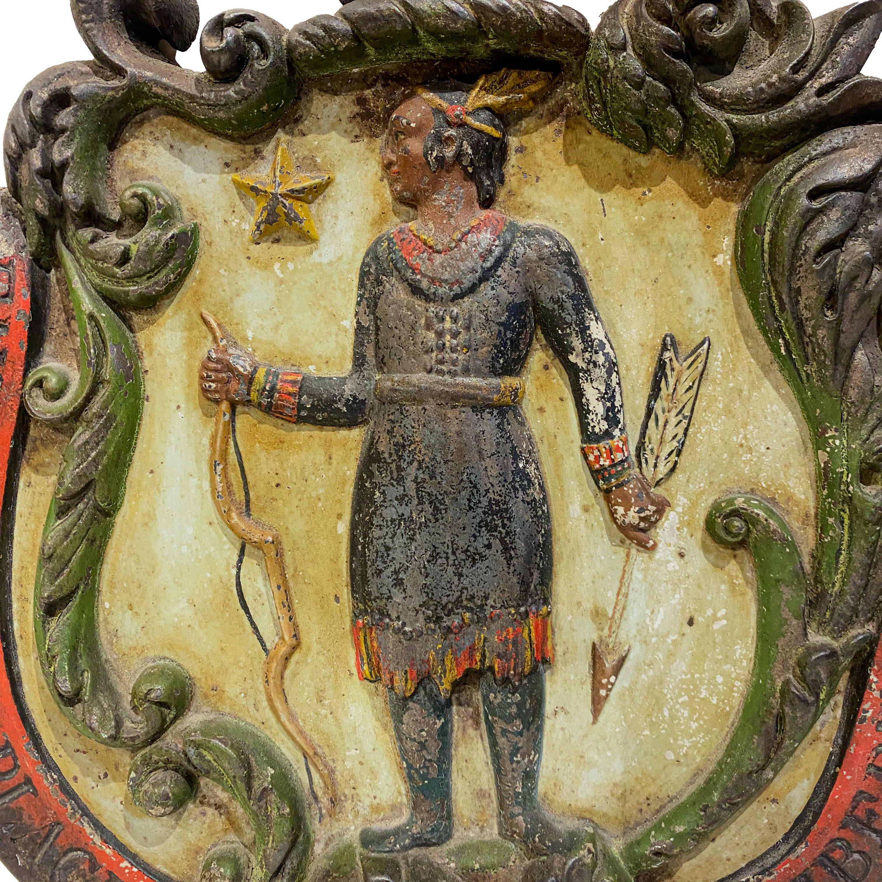 Architectural ornament, cast iron in the half round with a scrolled cartouche headed by a raised arm with sword enclosing a standing figure of a Algonquin Native American with bow and arrow, all above a banner with legend in Latin, Ense Petit