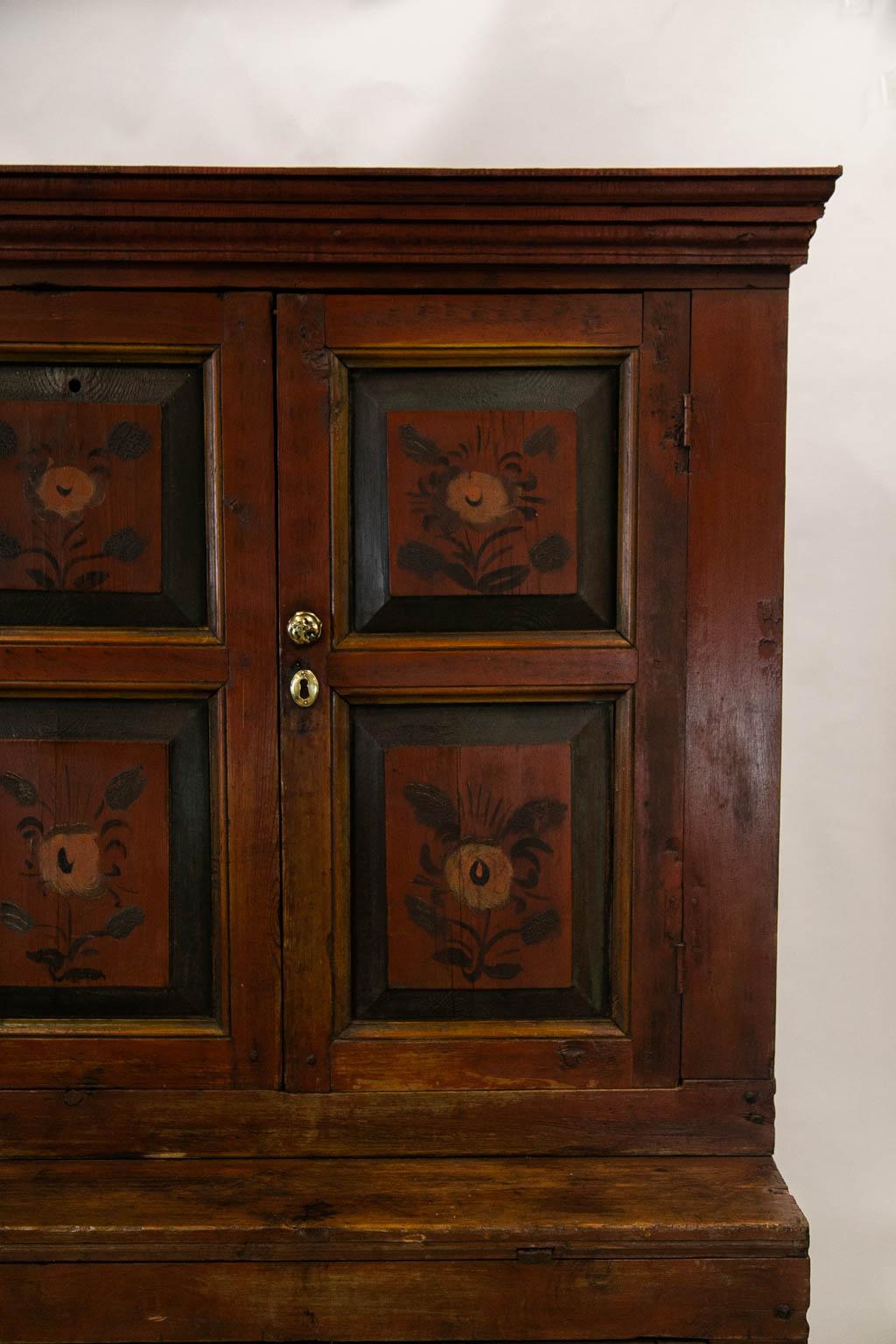 This cupboard has exposed peg construction throughout. The doors and central sections have raised panels framed with shaped moldings. The floral paintings are original. The shelves are fixed in the top and bottom.