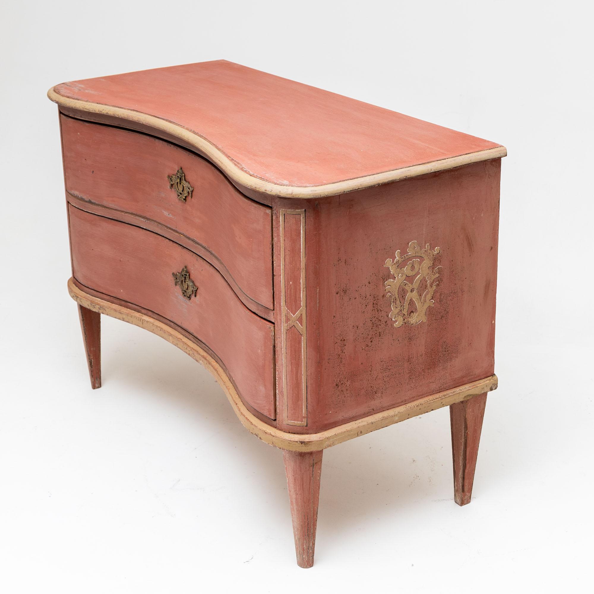 Elegant two-tier chest of drawers with bronze fittings, curved front and square tapered feet. The chest of drawers has been repainted and given an antique patina. The decorations are based on historical models. The brick-red colour is contrasted by