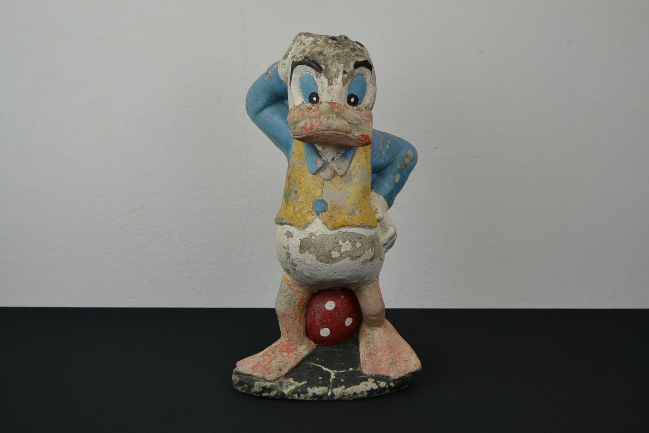 Concrete donald duck Statue. 
Donald Duck sculpture 
made of painted concrete - painted stone - composite stone.
He's wearing a blue and yellow jacket and is resting on a red and white mushroom.
During the years he got a charming old patina.