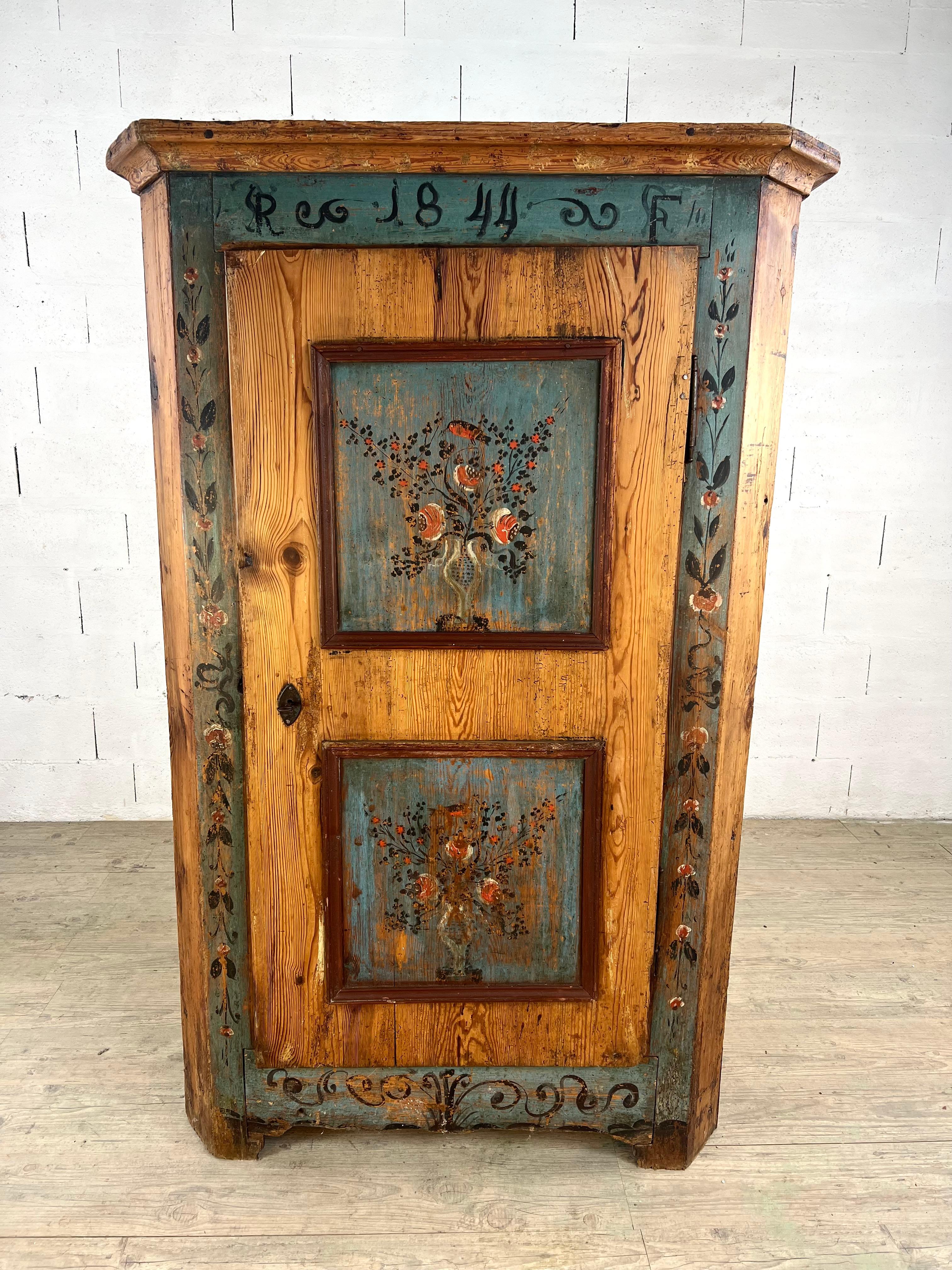 Charming painted pine cupboard, dated 1844, a fine example of Alpine / Rhenish folk furniture from the 19th century. This one-door bonnetière is decorated with two floral panels featuring stylized flower bouquets in vases on a faded blue ground,