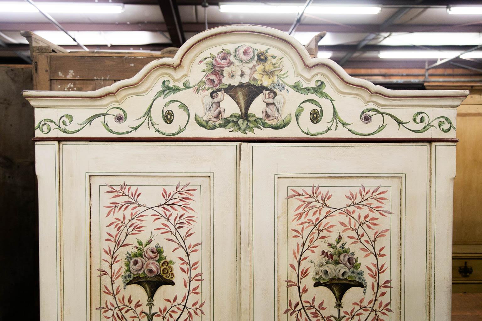 The doors of this armoire are painted with floral wreaths. The frieze is painted with floral arabesques and two cupids supporting a basket of flowers. The interior has a center divider. The right hand side has one shelf but has three additional