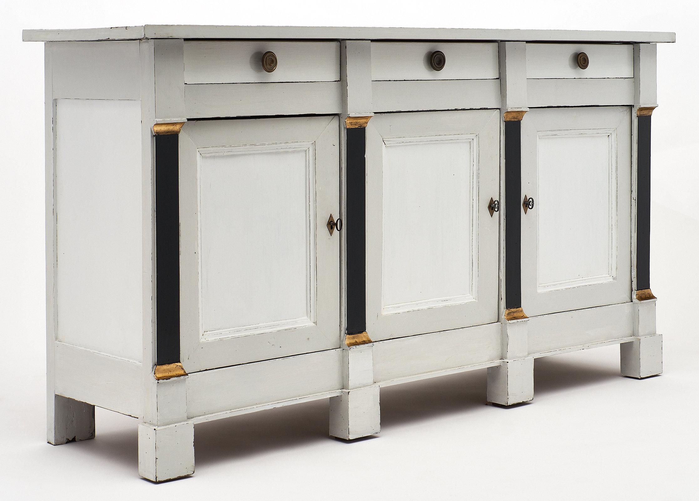 French painted Directoire style buffet made of walnut and patinated in a gray and white milk paint. This buffet features three doors with interior shelves and three dovetailed drawers. We love the ebonized and gold leaf details. Finely cast