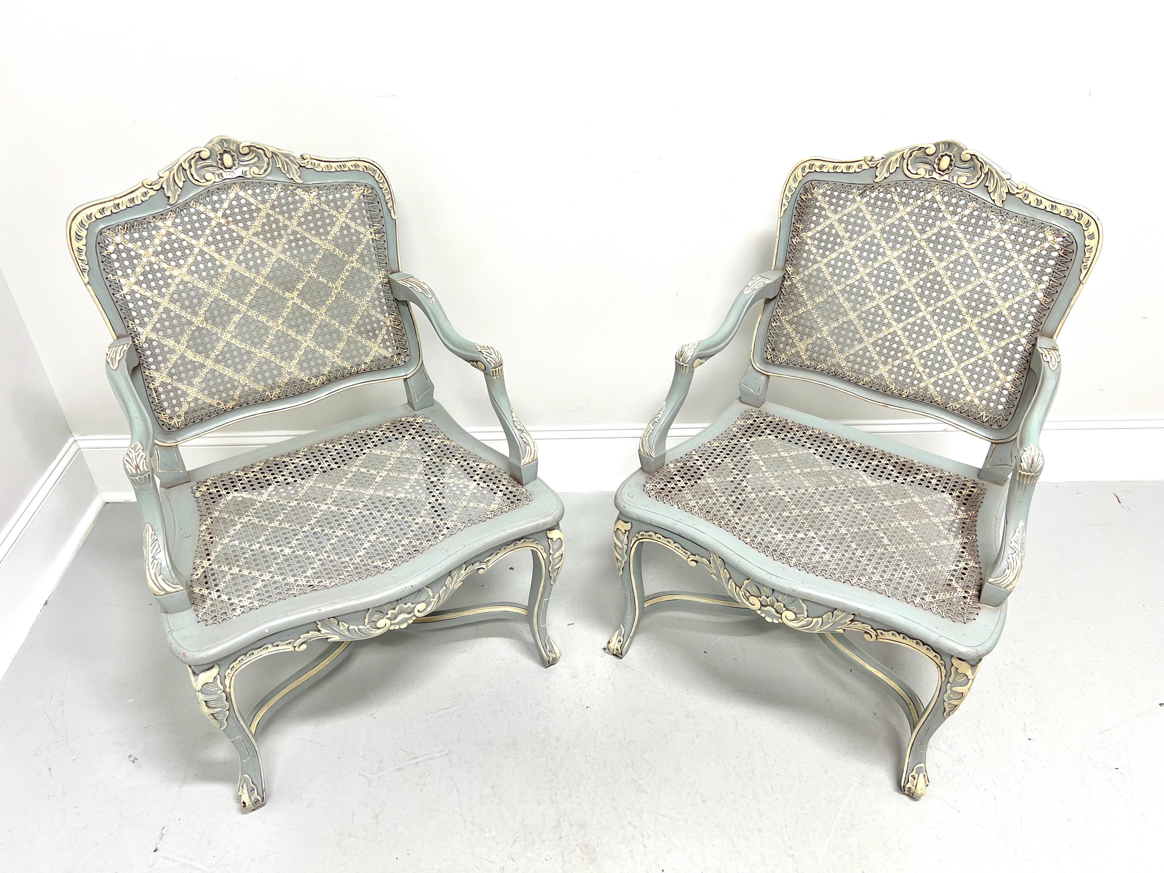 A pair of French Country Louis XV style armchairs, unbranded. Solid wood with a distressed painted finish of pale blue & ivory colors, decoratively embellished crest rail, woven caned backs, curved downward arms with embellished hand rest & arm