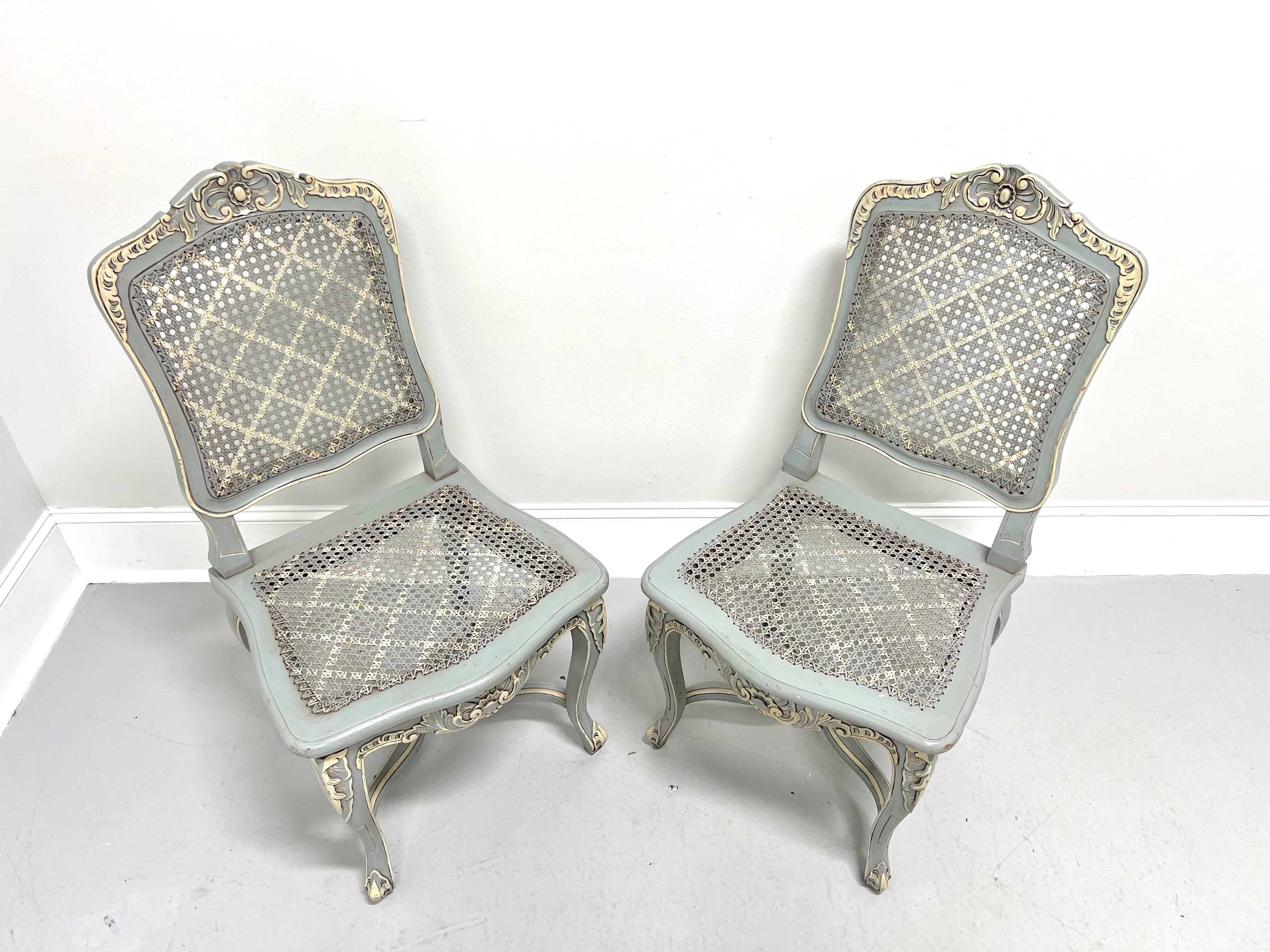 A pair of French Country Louis XV style side chairs, unbranded. Solid wood with a distressed painted finish of pale blue & ivory colors, decoratively embellished crest rail, woven caned backs, woven caned seats, decoratively embellished apron &