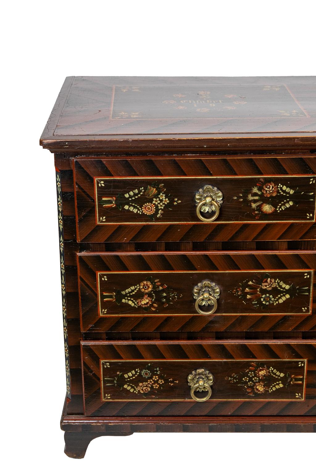 Painted European three-drawer chest, the top is faux painted to simulate herringbone banding. There are two floral cartouches on the top and each of the three drawers, dated 1900 on top.