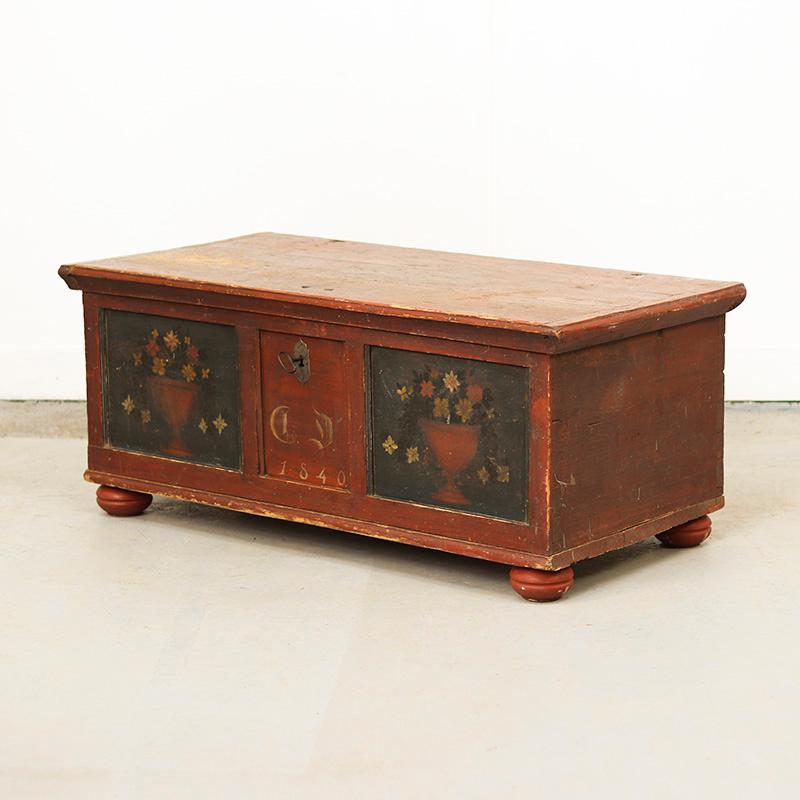 Beautiful painted bridal chest from Germany, specifically from the Franconian Alb. The chest is painted in oxblood red and features beautiful floral decorations on the front panels. This old paint is quite worn and weathered, giving it a rustic and