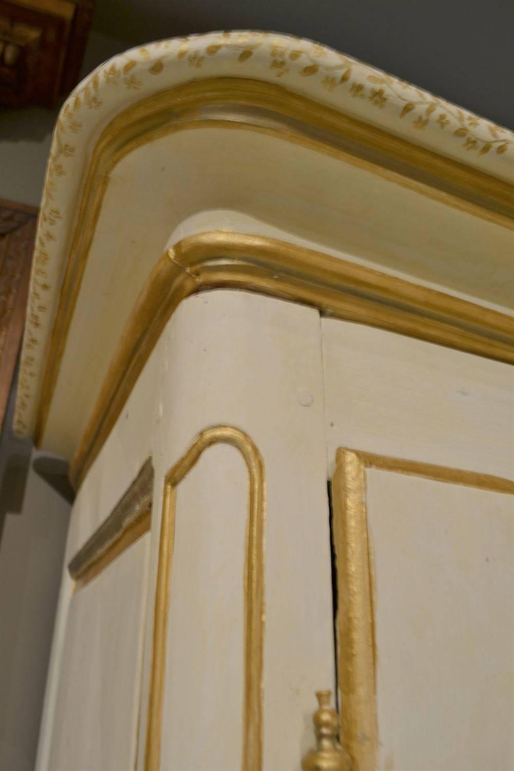 This early 19th century oak armoire features a recent decorative painted finish. The designs were done in metallic gold and silver paints, and the cabinet has been distressed and glazed to look old. The piece has wear typical of its age and the