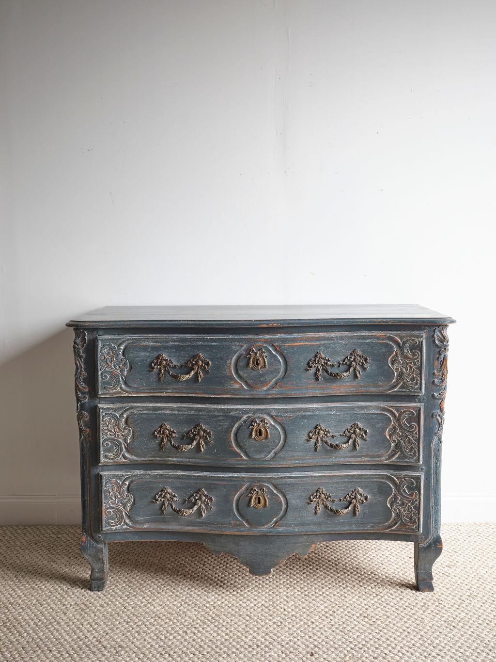 This is an incredible blue painted French commode. The year it was painted is unknown, but seems to be in the same period of the chest since the paint is aged. The lovely hardware is ornate and original. There are unique wood carved details along