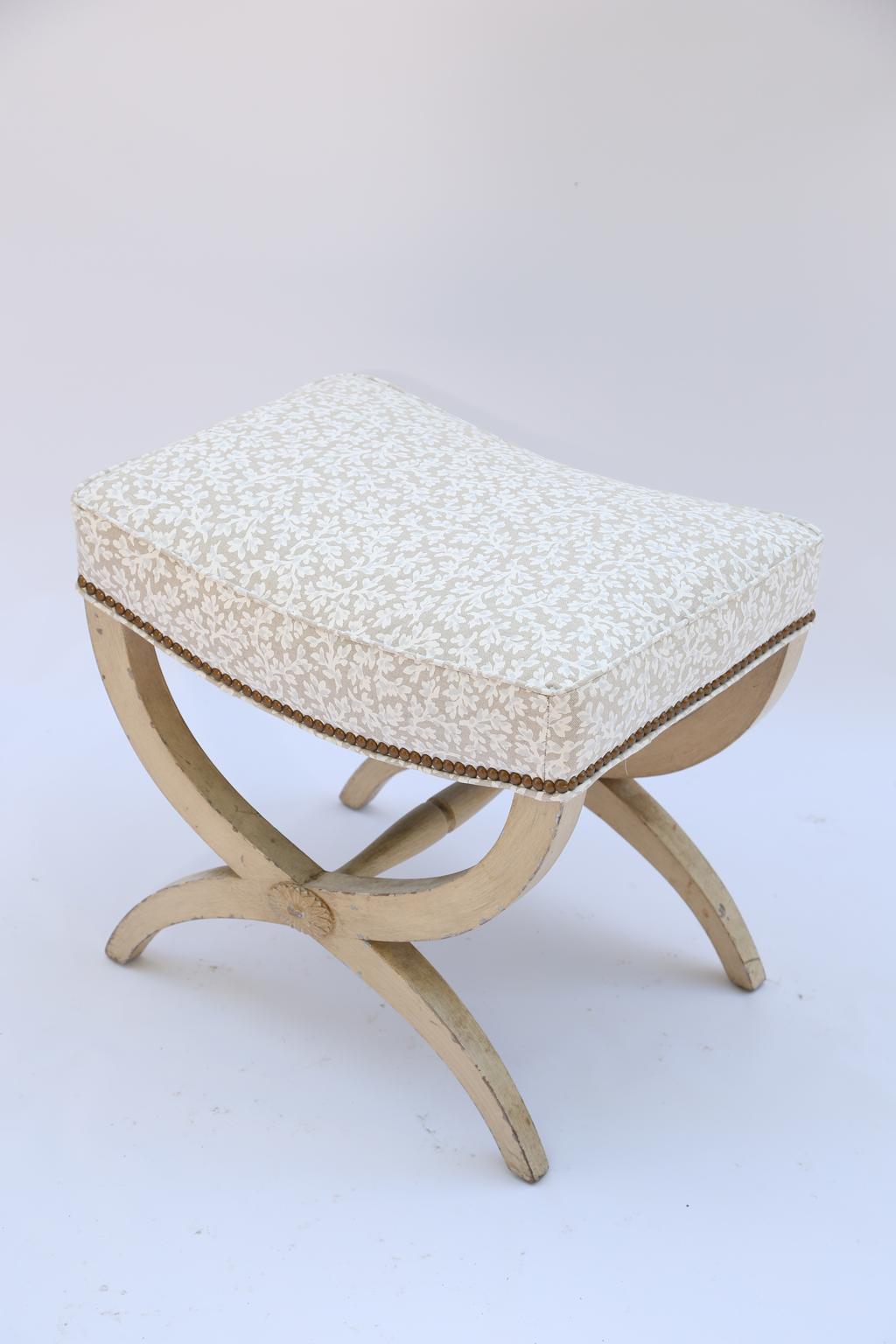 Stool, having a rectangular boxed seat, on painted base showing natural wear, its Curule form legs joined by turned stretcher, and rosette. Upholstered in vintage printed-linen, with nailheads.

Stock ID: D1758.