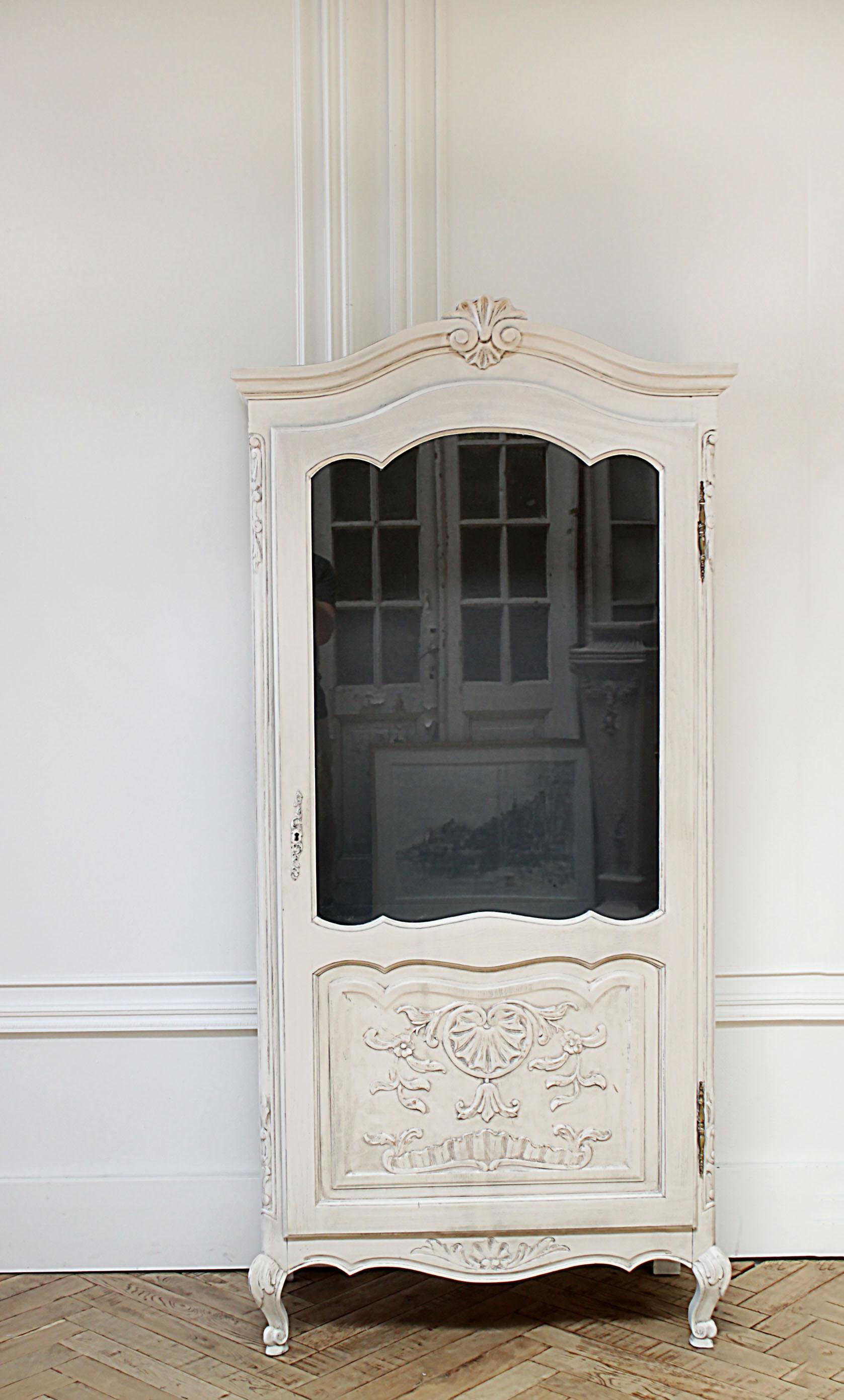 Painted Country French style display cabinet
A soft oyster white finish, with subtle distressed edges, and beautiful carved floral and shell motif.
The inside is painted in a dark grey, and has 1 fixed wood shelf, and 2 glass shelves. Door opens