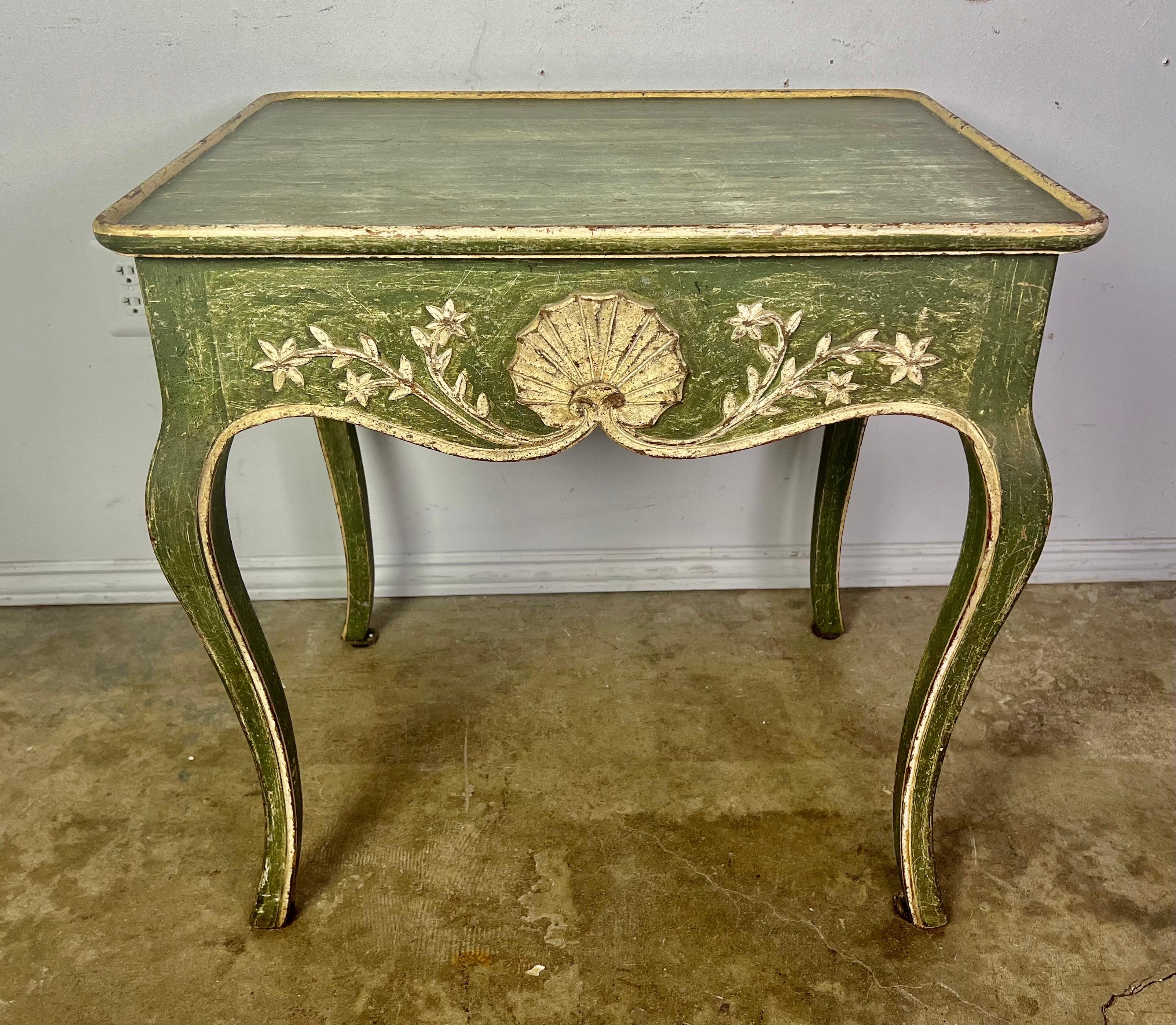Early 20th century green painted side table with single drawer on the side. The table is beautifully decorated with a center shell design flanked by scrolled flowers. The finish is worn to perfection. The table stands on four cabriole legs that end