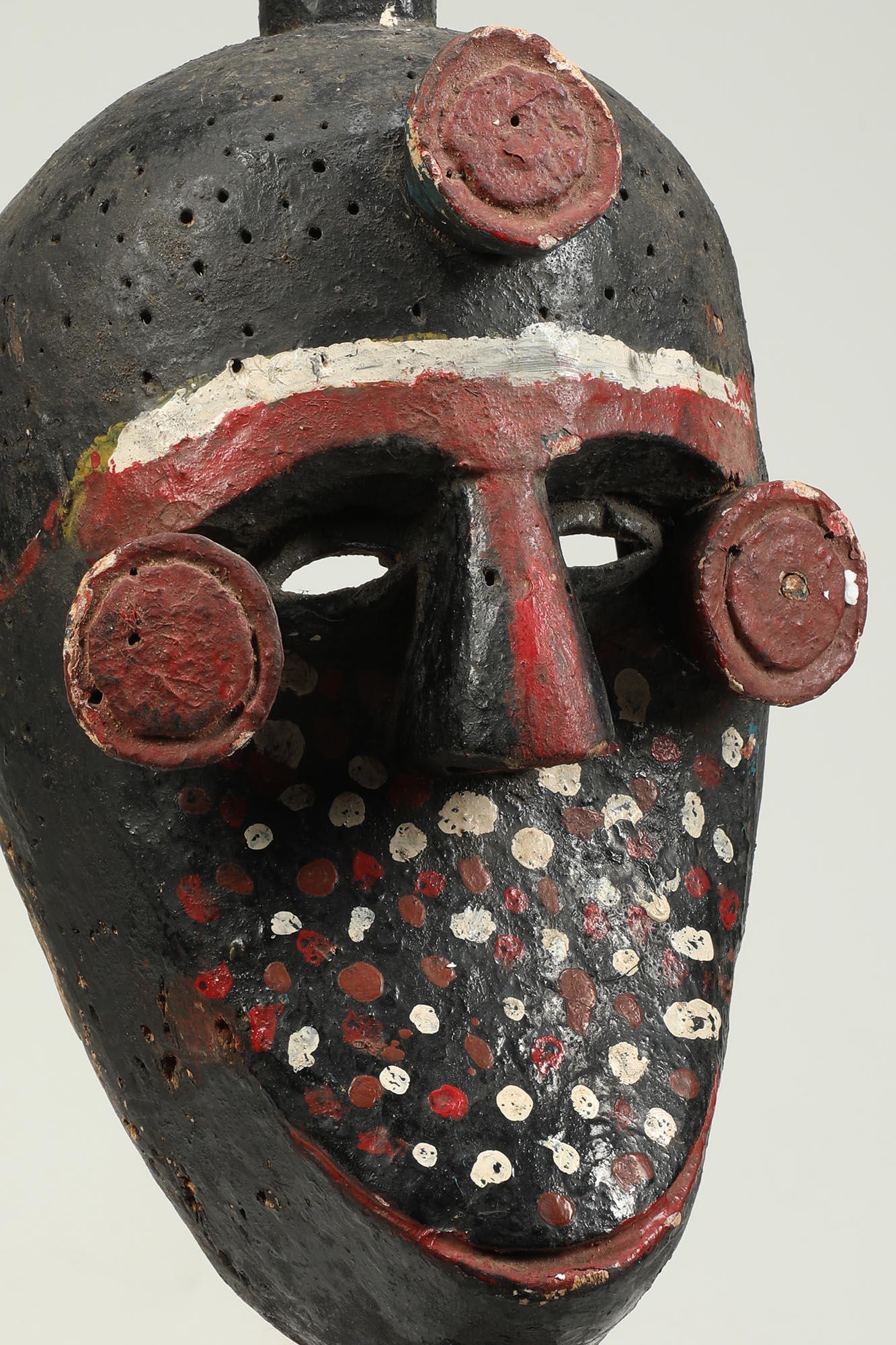 Fine Painted Ibibio Polychrome Mask with Figure on Top, Nigeria Africa. Expressive small figure on top with one hand on top of head, other holding stomach. Circular projections at the corners of the eyes and the center of the forehead. Old painted
