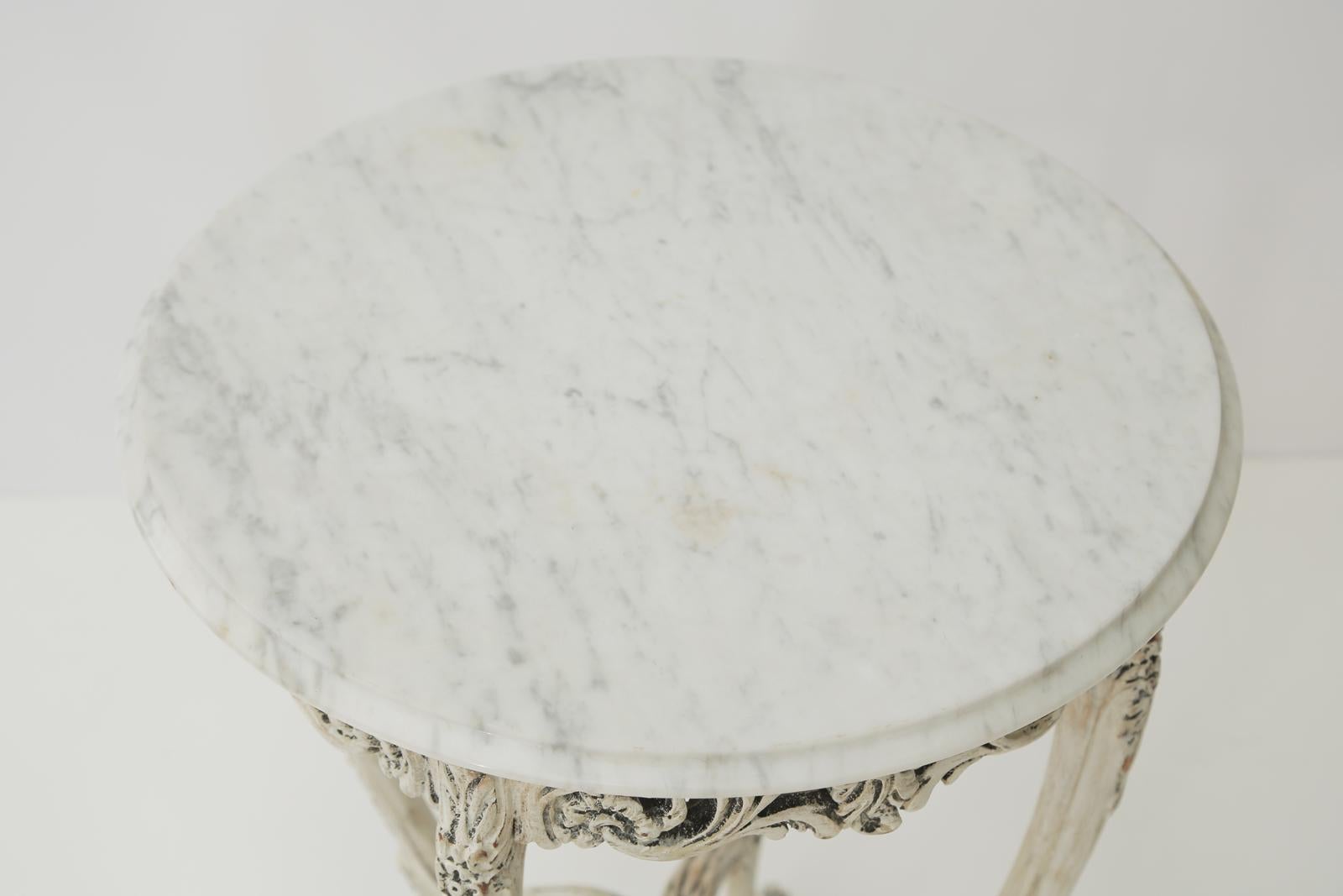 Painted occasional or end table, having a round top of Carrara marble, its pierced apron carved with foliate scrollwork, raised on four, round, bowed legs, each headed with a rosette and drape, joined by a shaped stretcher, ending on scroll toes and