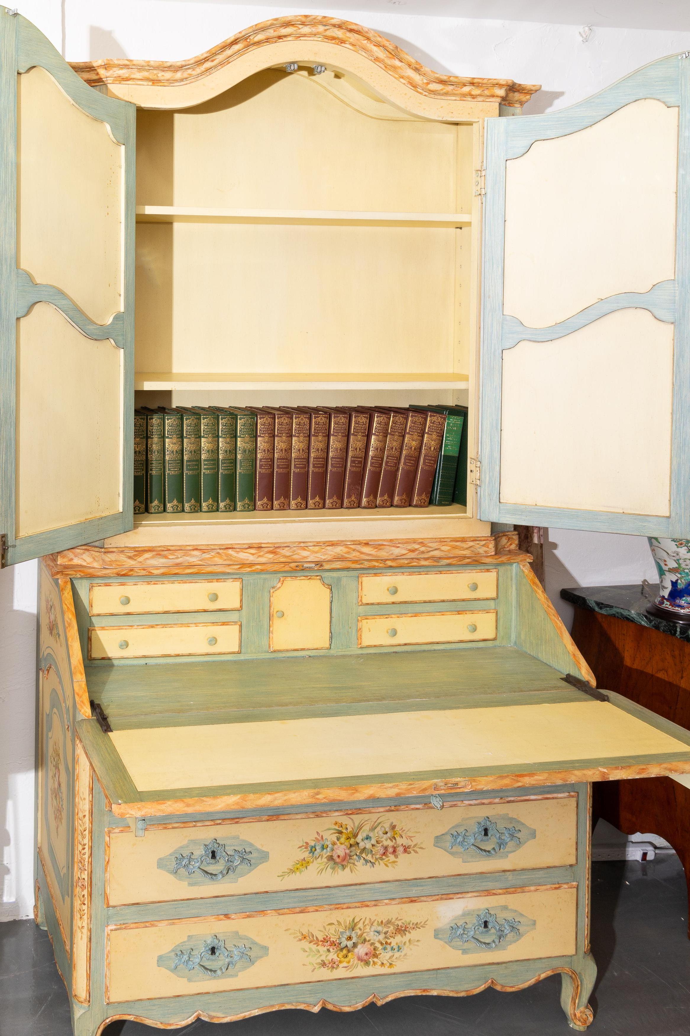 This is a lovely, decorative Italian secretary, painted overall with floral sprays against a pale yellow ground with light blue demarcations. The dome cornice is over two paneled doors. The bottom section has a slant front over three graduated