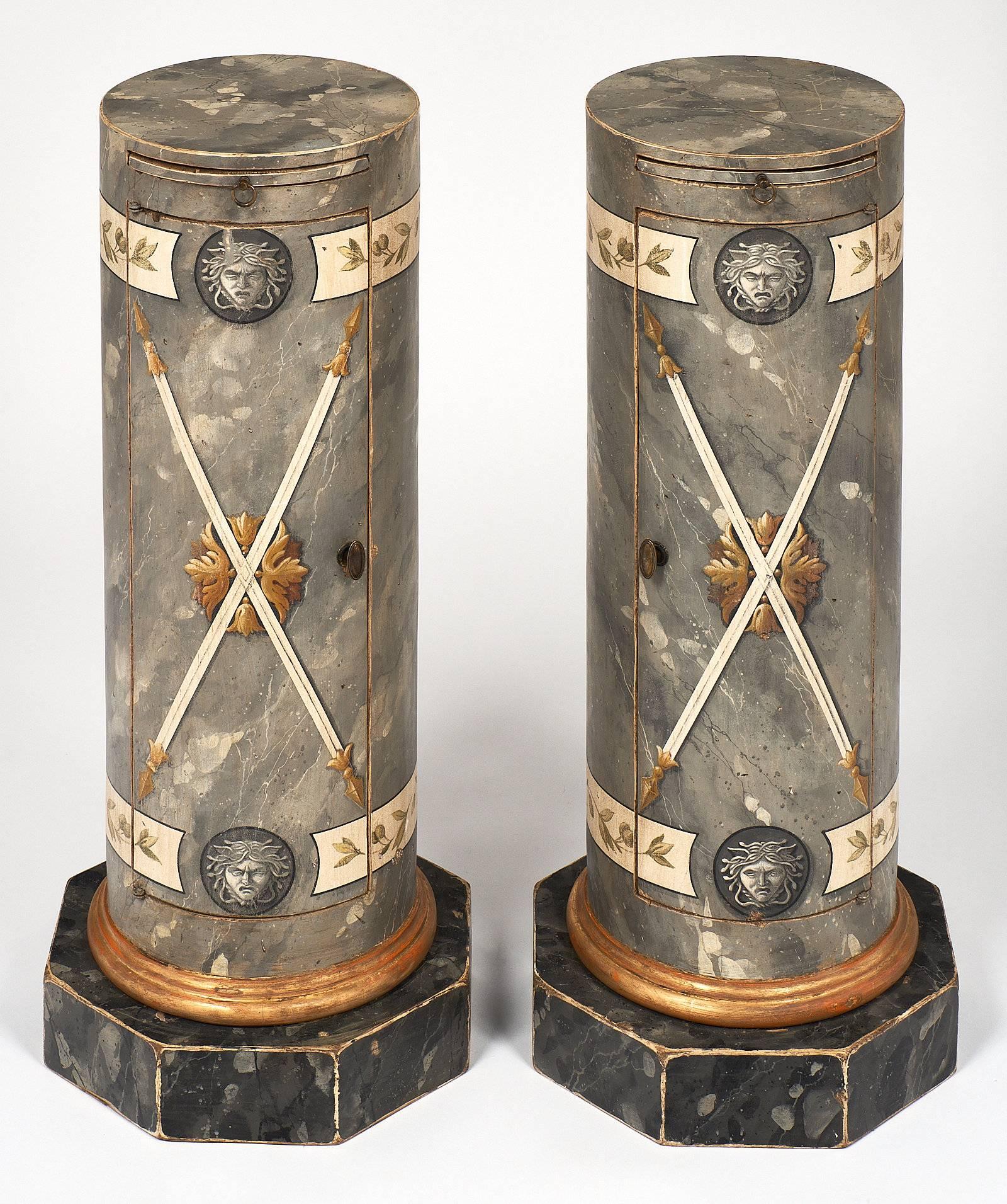 A pair of faux marble Somno columns, made of fir with hand-painted and gold leafed with a decor of Medusa, laurel reefs, and Romans javelins. Set on an octagonal base, each piece features a curved door that opens up to a shelf as well as a pull-out
