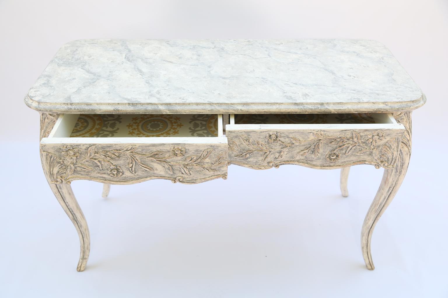 Writing desk or console table, finished on all sides, having a painted finish, showing natural wear, its molded, rectangular top on serpentine apron, hand carved with scrolling acanthus, containing double drawers, raised on scallop shell-headed