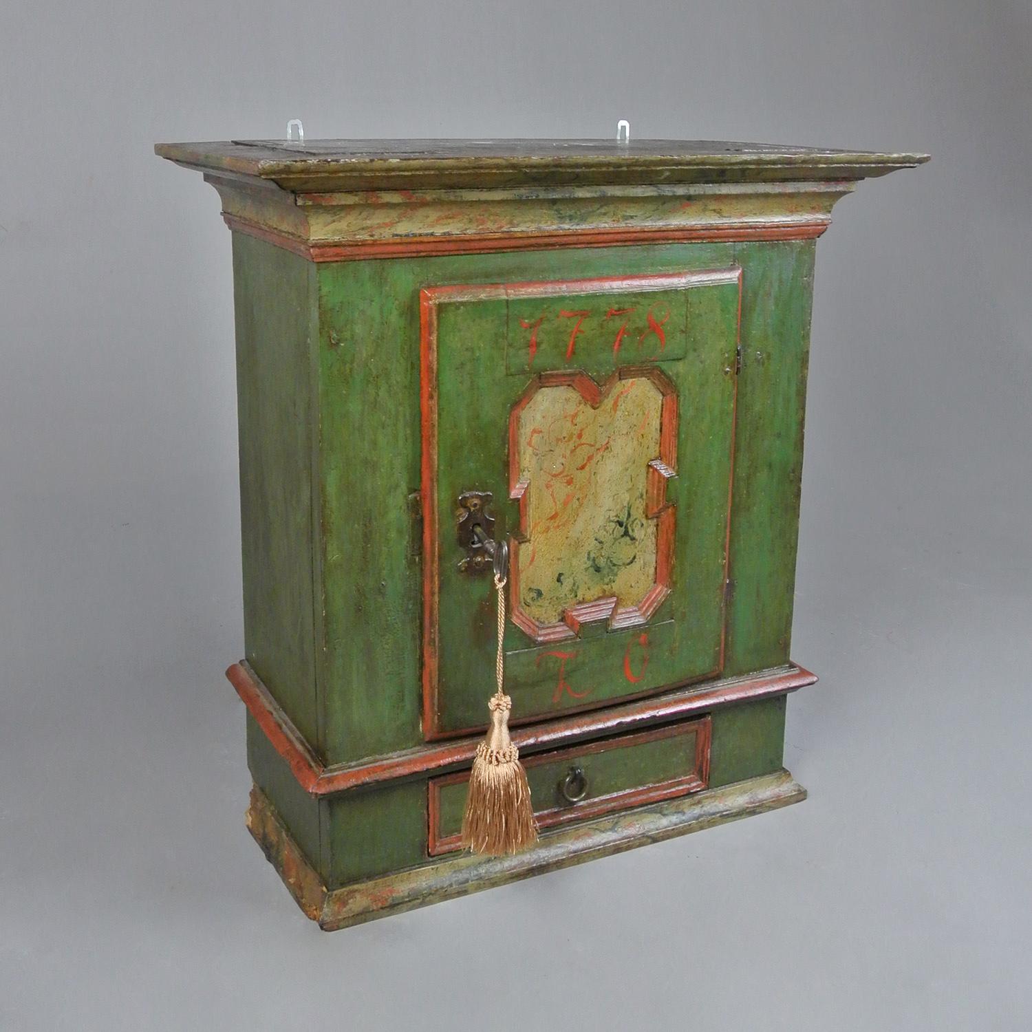 A charming 18th century wall hanging cabinet, Swedish, dated 1779 and with the initials L.O. Original painted finish in a soft green with orange highlights and with decorative foliate panel to door and the same pattern painted to the cornice and