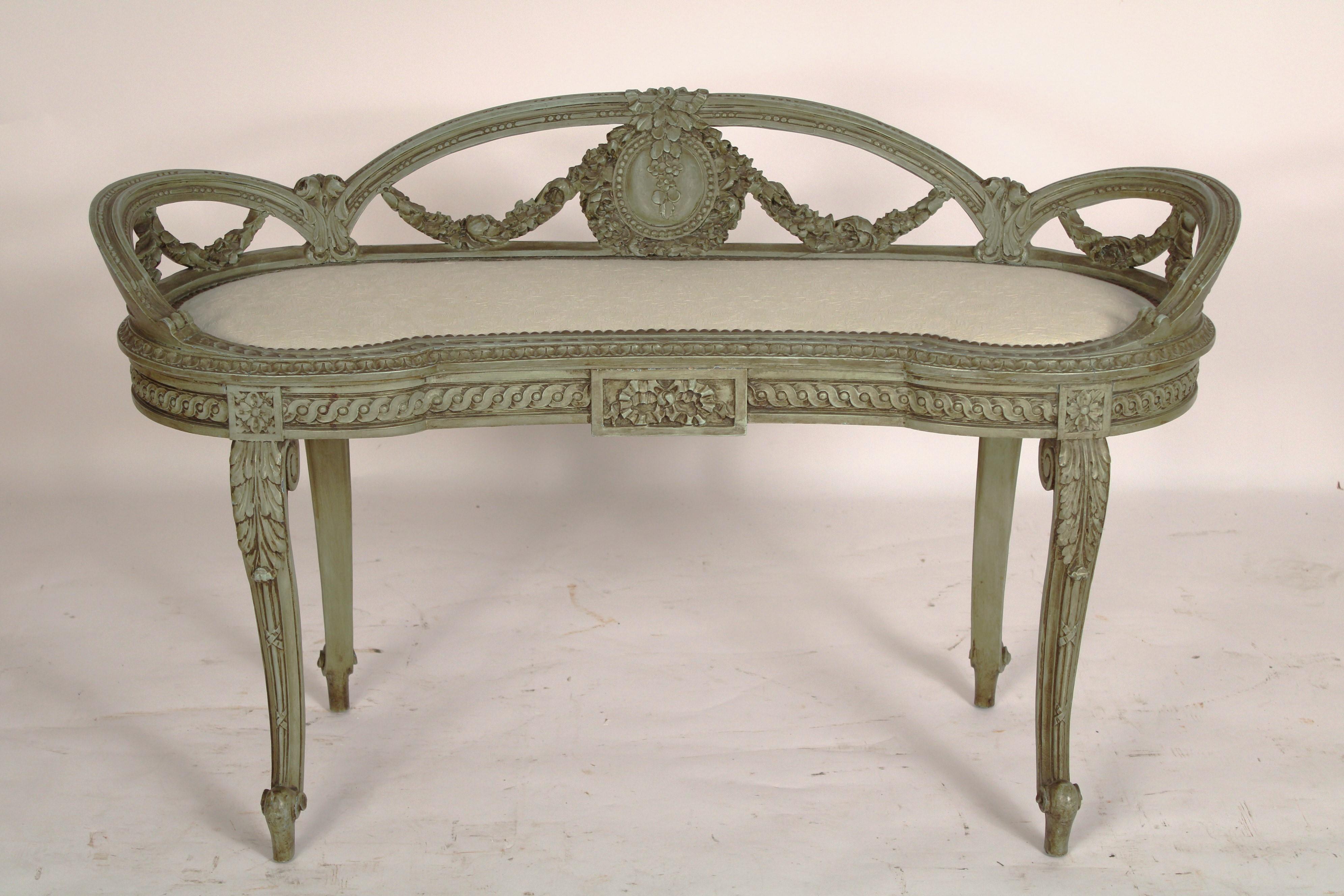 Louis XV / XVI transitional style green painted bench, circa 1930's. With a slightly raised back with carved swags, a kidney shaped upholstered seat 
with brass nail heads, a gouilloche carved apron, resting on 4 cabriole legs with acanthus carved