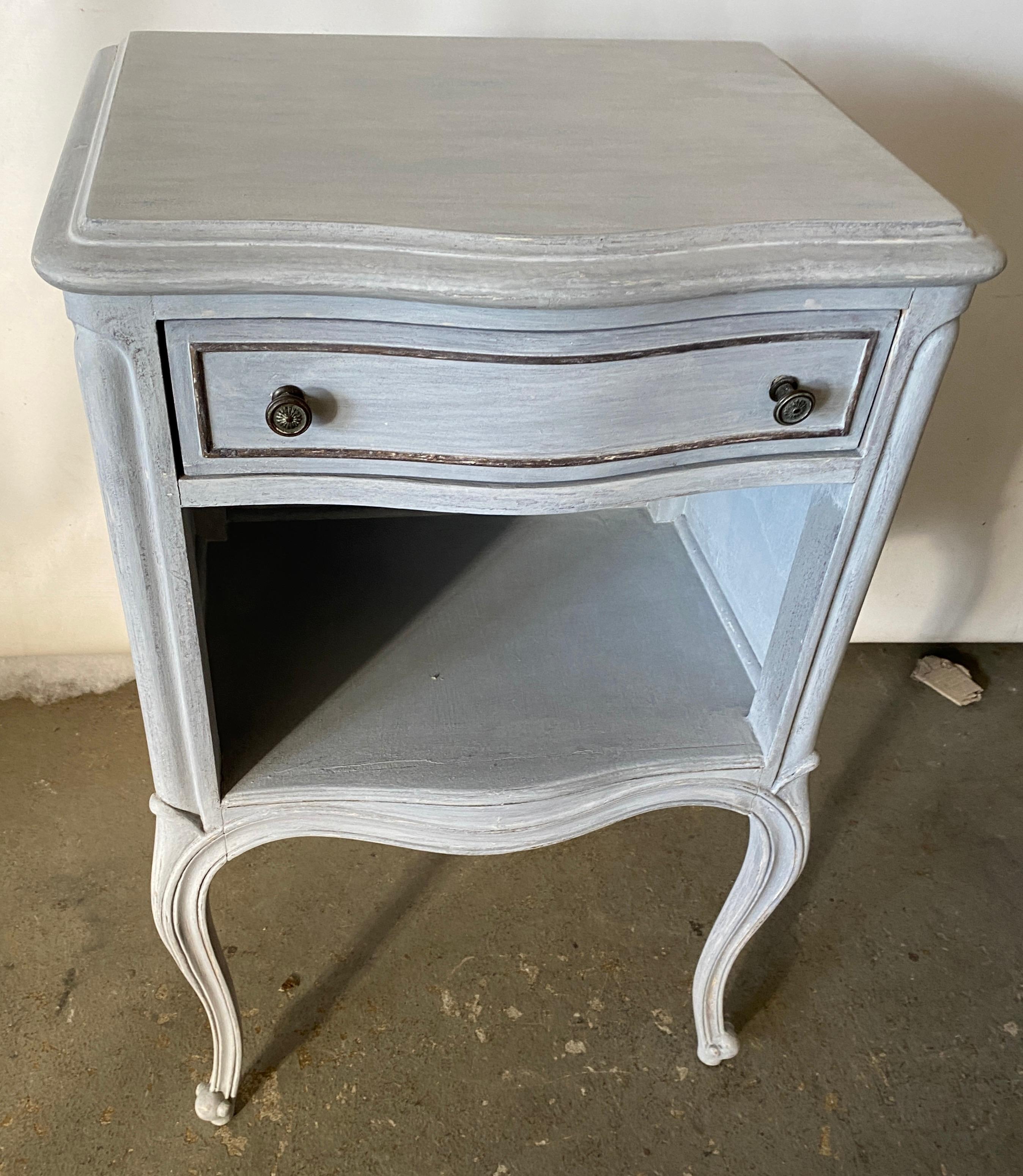 The grey and gold gilt painted metal night stand has an open upper shelf with a pull out tray and a cubby hole or lower shelf for more storage. This night table or stand will fill the bill if you are searching for a Swedish Gustavian, neoclassical