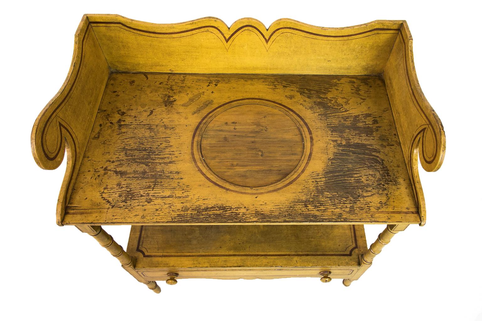 This painted one drawer faux bamboo table has a shaped gallery on three sides. The top has well weathered paint. The center hole, which originally held the wash basin, has been filled with wood to blend in with the rest of the top. The top, back
