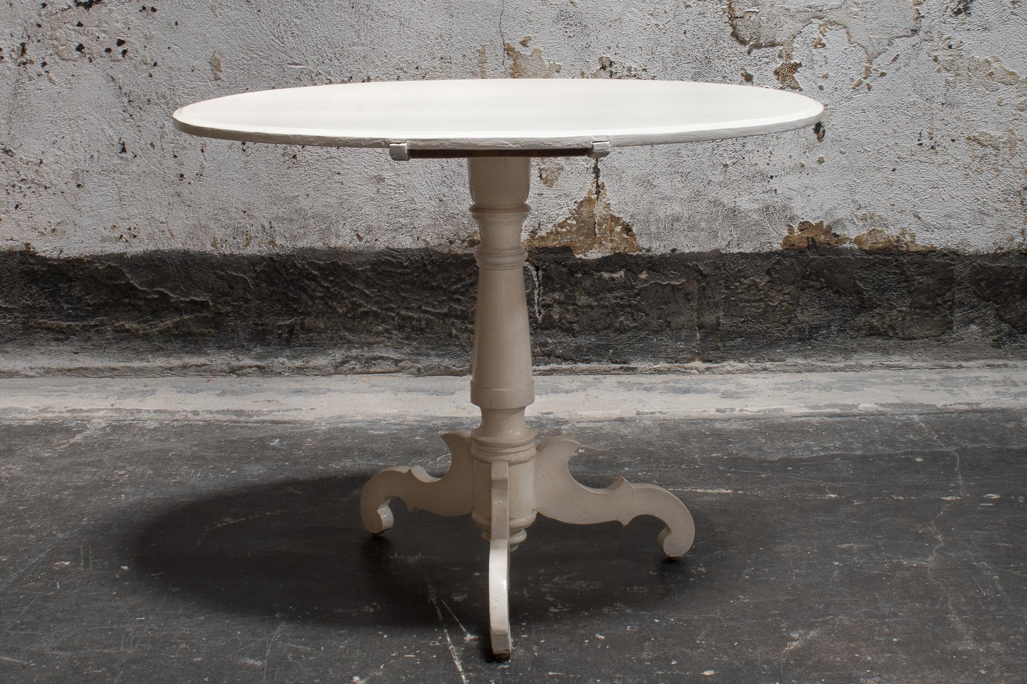 Oval tea or game table was made in the early 1900s. This handsome table features a simple circular surface with a hand-turned center post on a three-leg pedestal base. Painted in soft off-white, table has patina that points to its early 20th century