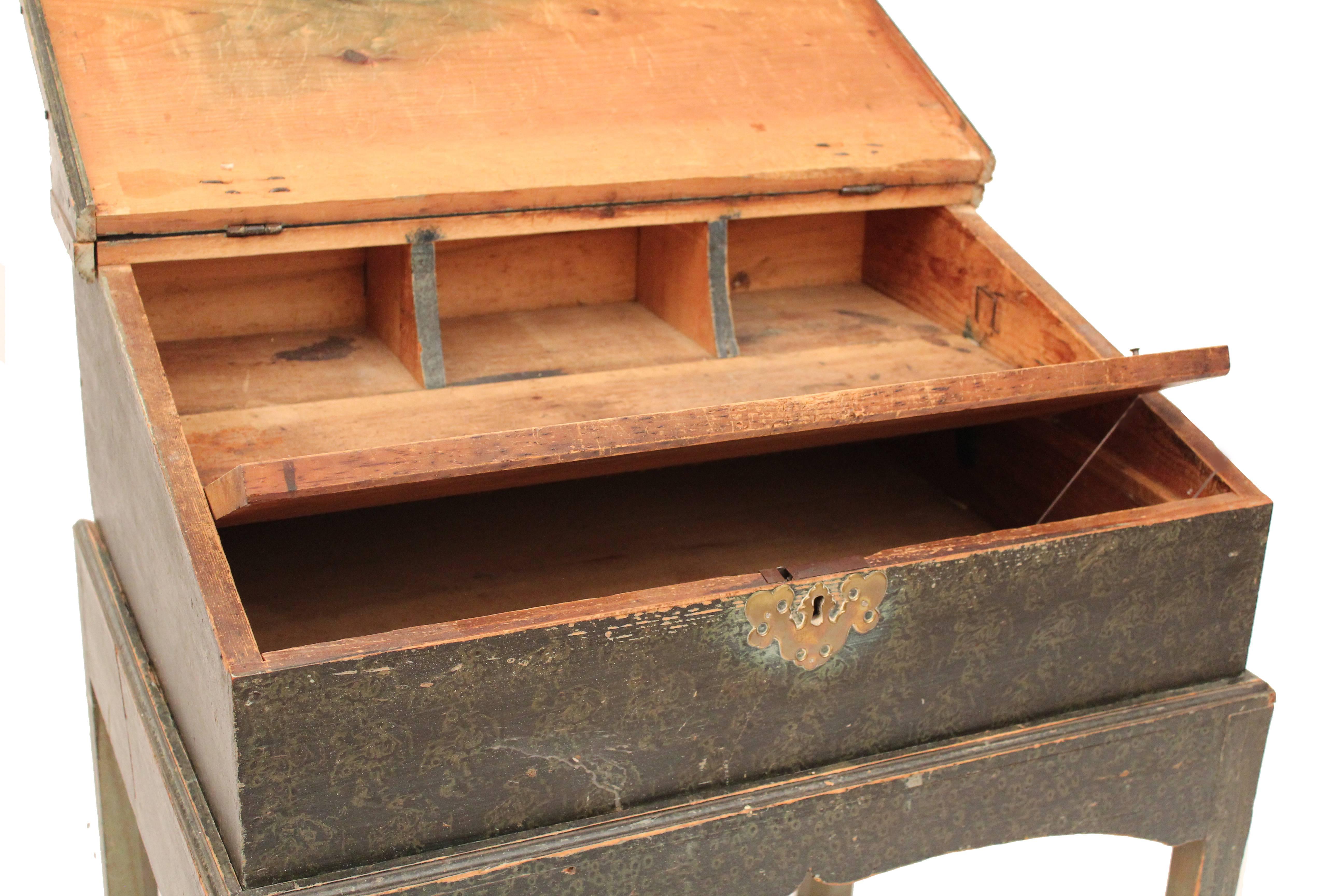 A pine New England desk on frame with original blue grained paint and iron butterfly hinges. It has a lift lid with four interior compartments, box stretchers and straight legs.