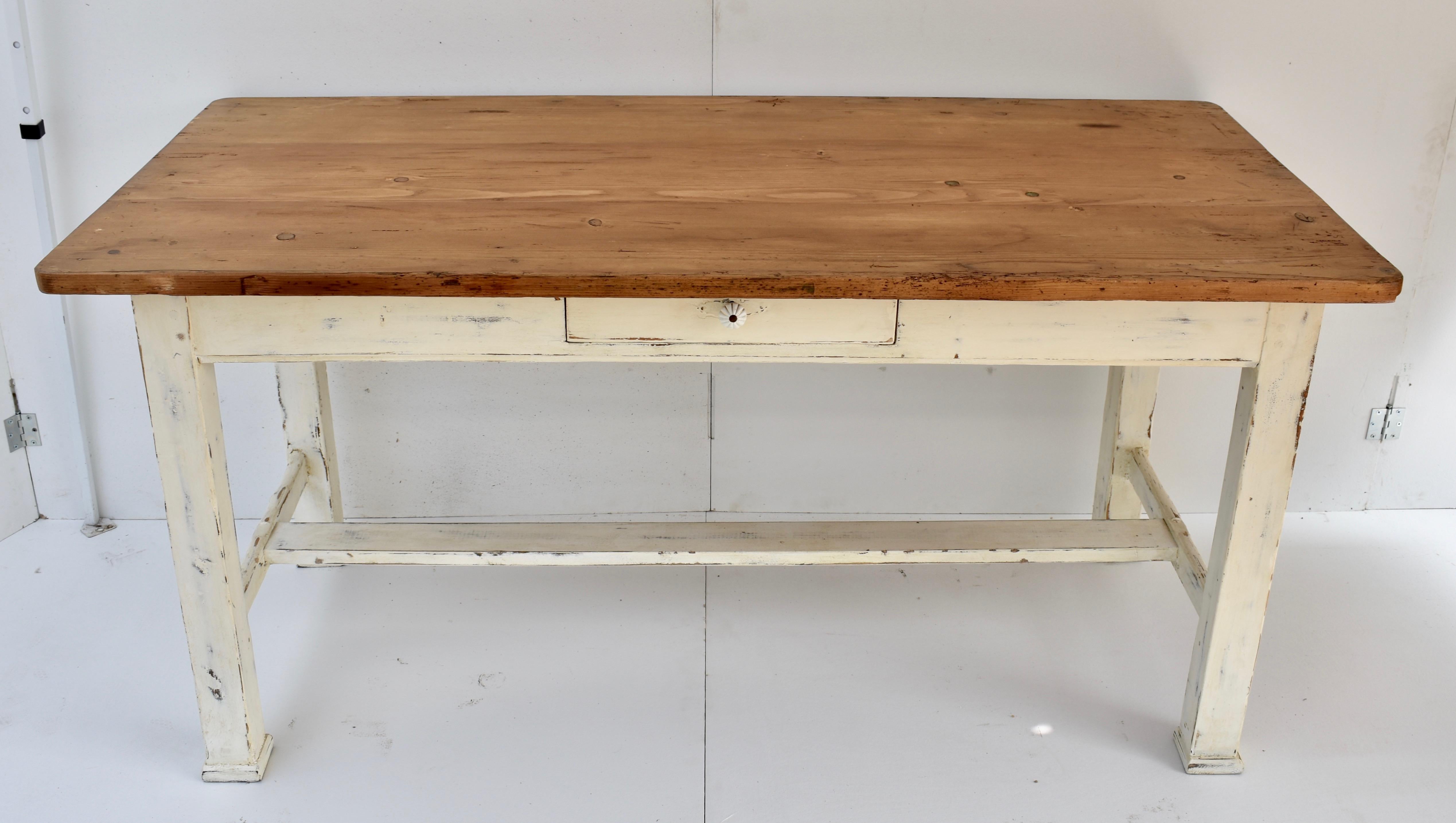 This attractive farmhouse table has a thick richly-colored pine top, sturdy 3” square legs joined by well-worn stretchers and a single central hand-cut dovetailed drawer with a traditional ceramic knob. In old white paint worn through to blue and to