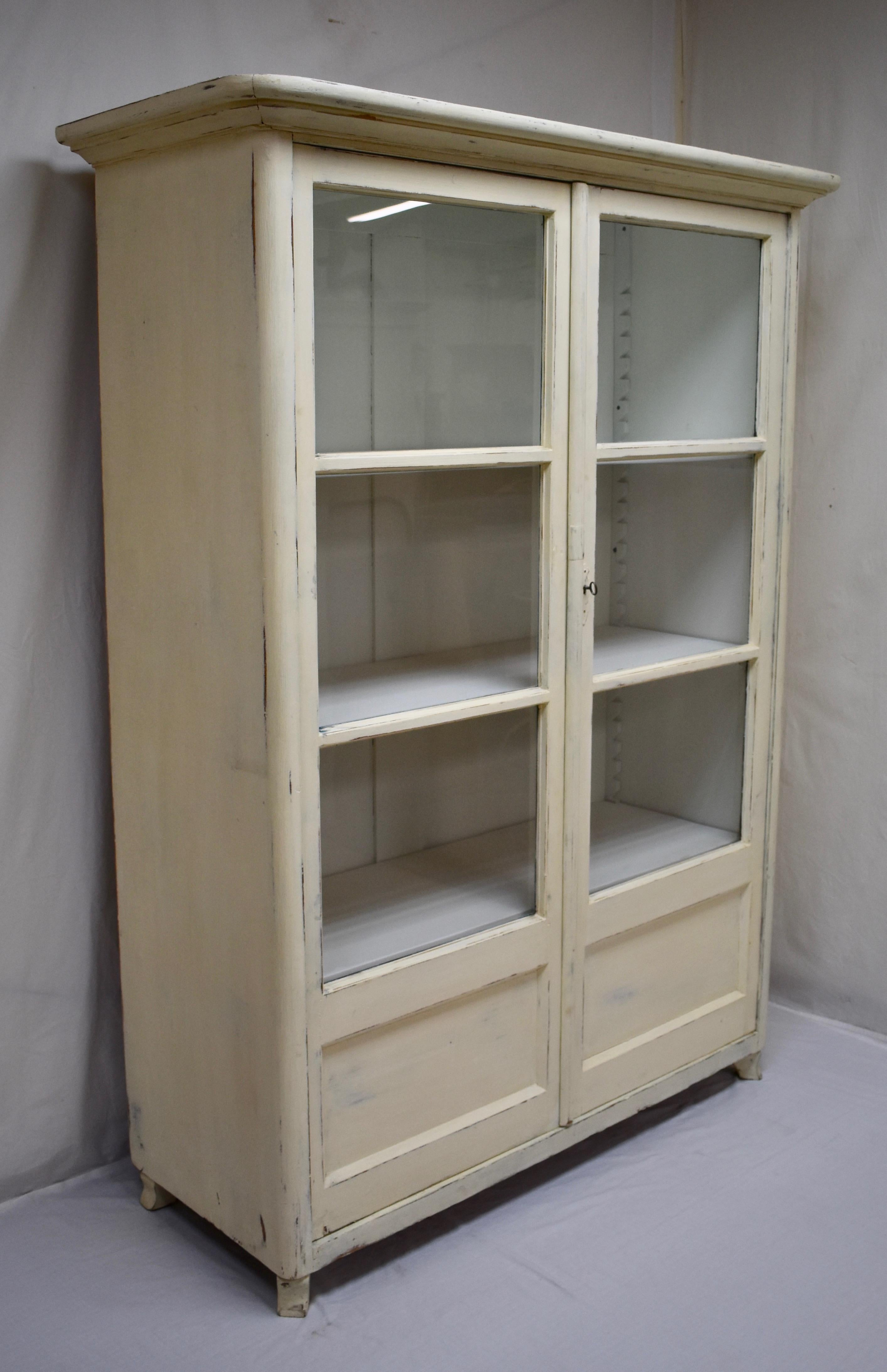 This is a sturdy two-door glazed cabinet built from 1” thick yellow pine. Beneath a bold crown molding are two pivot-hinged doors, each with three glazed panels with a blind panel at the bottom. The front corners of the cabinet are gently rounded to