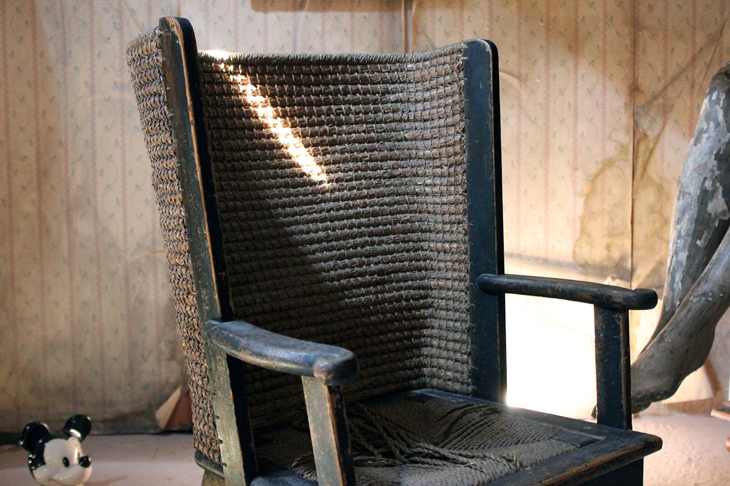 The curved woven straw back with upright supports issuing open arms with scroll terminals, the drop-in seat raised on square tapering legs, the black painted whole designed by Reynold Eunson and made by D.M. Kirkness, Kirkwall, Orkney, Scotland and
