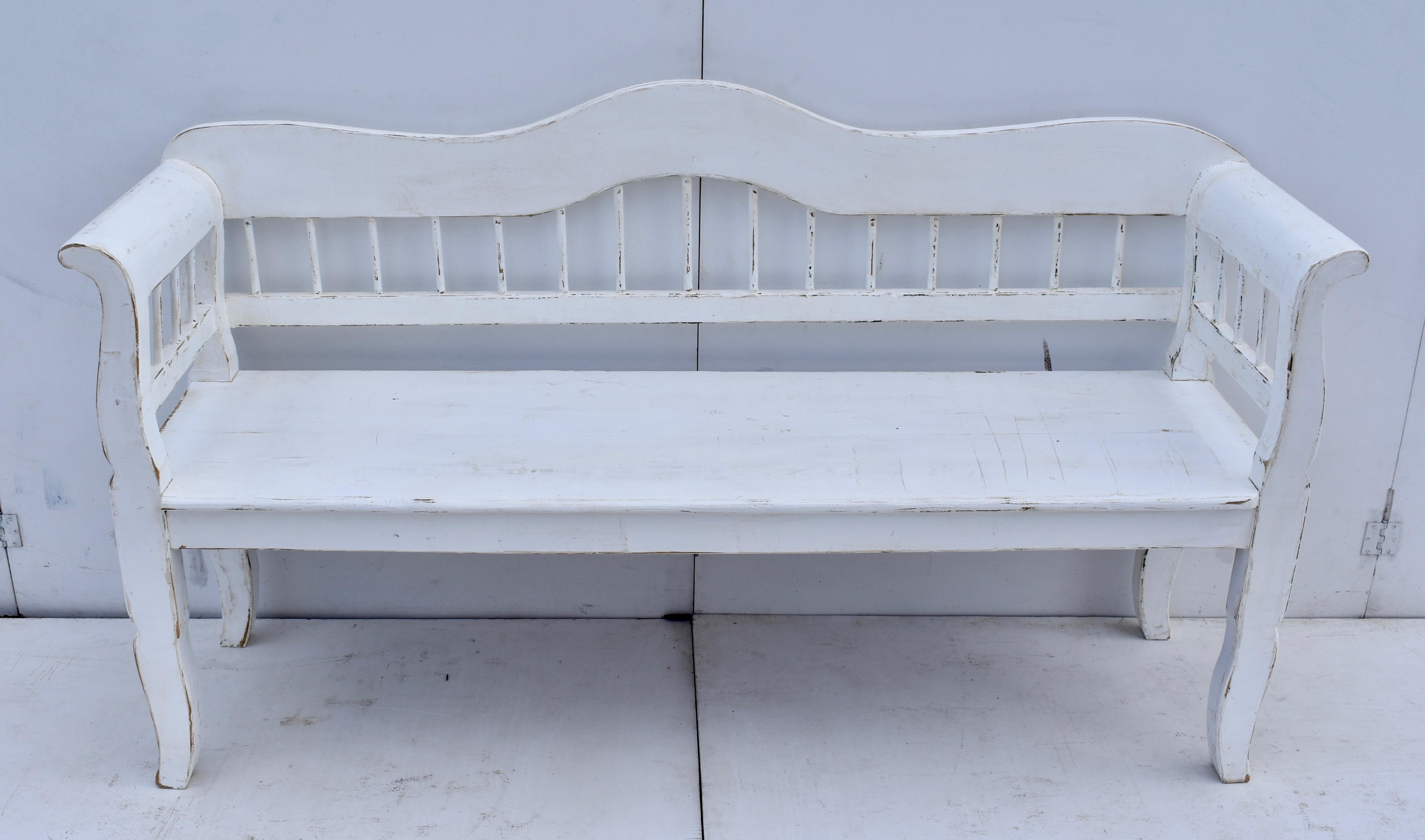 The thick back rail of this Central European Settle is a little raised at the ends and boldly arched in the middle and with the straight lower rail encloses a row of simple turned spindles. The integral scrolled arms and curvilinear legs are joined