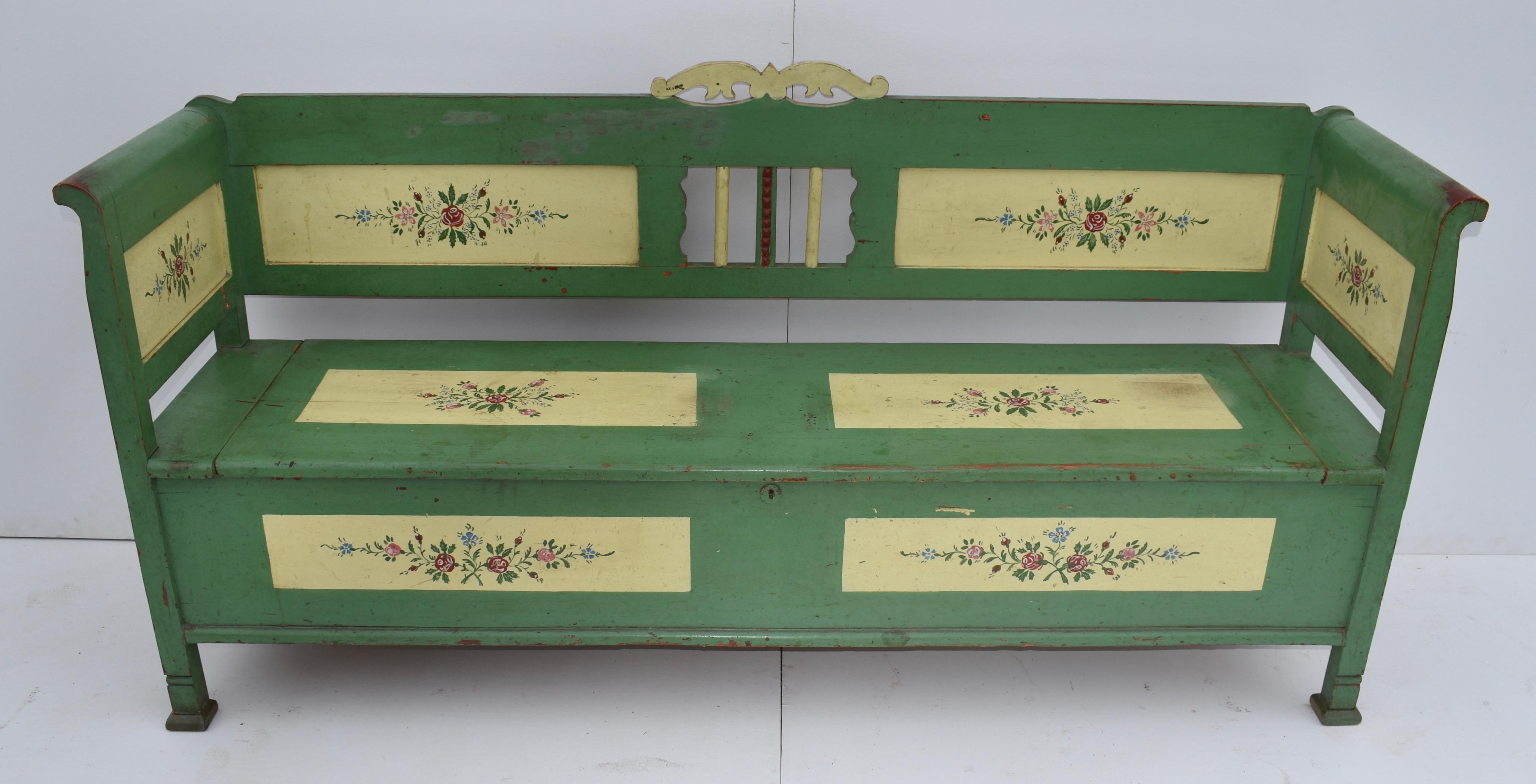 A fretwork crest mounts the back rail of this very clean, beautiful box bench, repainted with a green ground on red stain. Two flat panels with recently executed folk art floral decoration flank a central opening with three spindles, the centre one