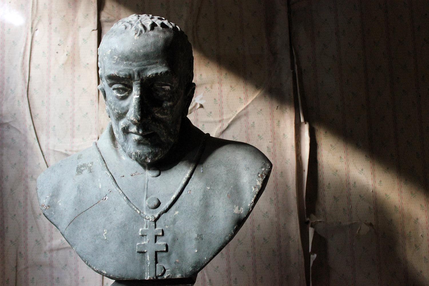 The large late Victorian plaster library bust depicting an unidentified priest, of middle to late age, possibly modelled on an Elizabethan, wearing a ceremonial robe with the pectoral cross of lorraine, the whole on a stepped socle square base,