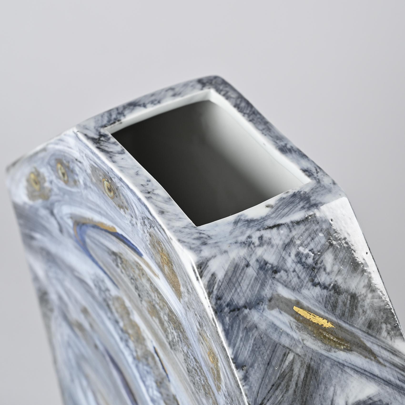 
Vaso poligonale in porcellana a colaggio, con decorazione dipinta e riflessi dorati. Ampie pennellate bluastre e grigie animano la superficie con un gesto libero ed espressivo, rivelando un approccio pittorico al materiale.

Quest'opera proviene