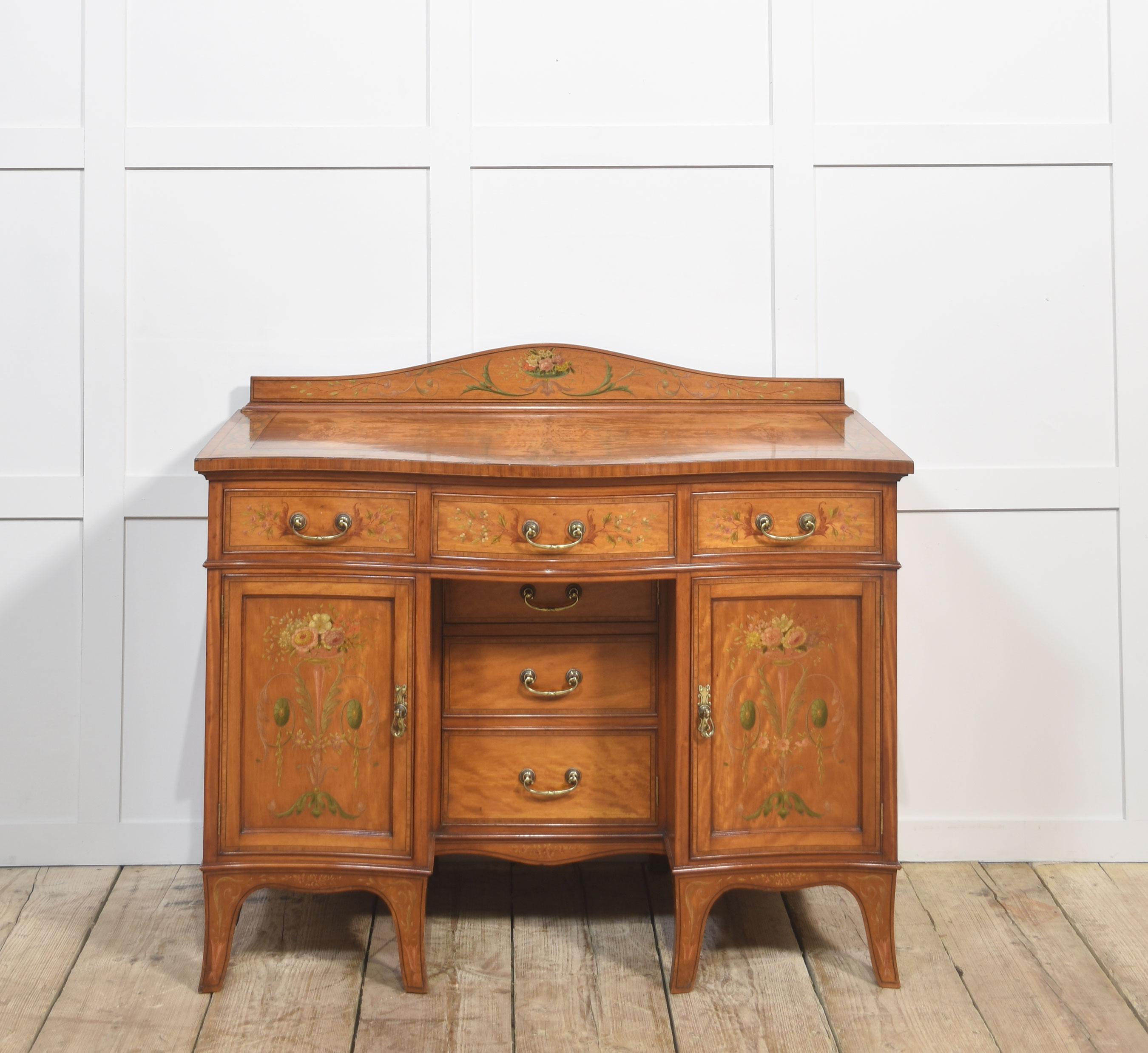 A refined late 19th to early 20th century satinwood dressing table, beautifully hand-painted in the Sheraton Revival style. The serpentine top is bordered with delicate floral garlands, while the drawers and cupboard doors are adorned with finely