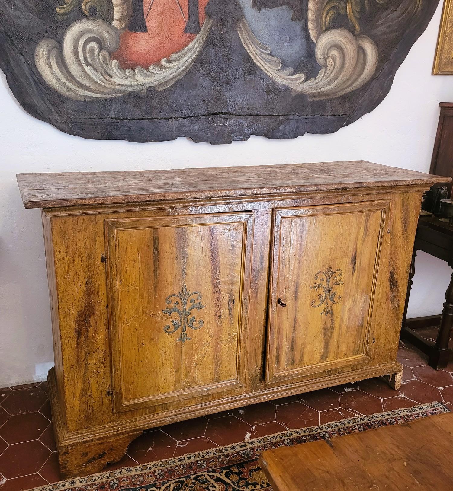 Large 2-door sideboard in wood painted in yellow/ochre tones with a stylized foliage or flower decoration in blue on the doors and sides.  

 Tuscan work from the 17th century, some repainting (and blue motif added later), wear and missing parts