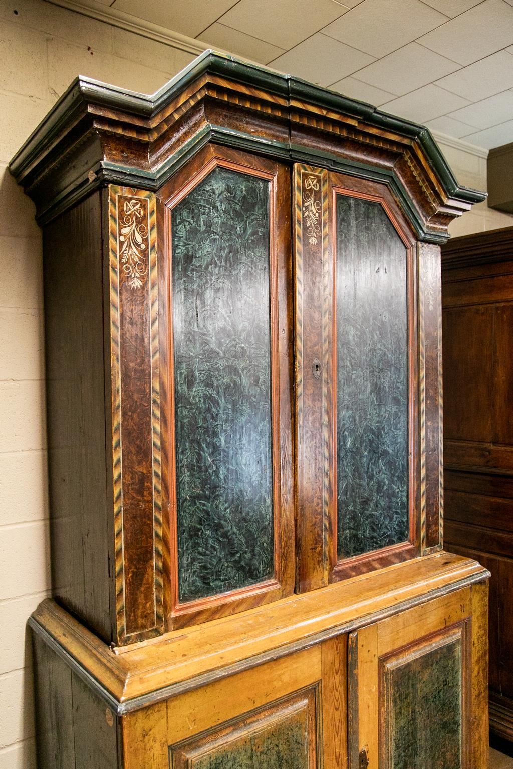 Unique painted step back cupboard has signed initials and is dated 1839. It has sponge painted panels with bowed ribbons suspending floral designs. The center and side panels are painted with brown, green, and beige stylized herringbone, with a