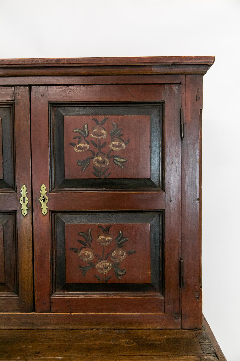 This step back cupboard has raised panel doors on the top and bottom sections. The upper doors are painted with floral motifs. The lower drawers have the original red paint. There is exposed peg construction throughout as well as large dove tail